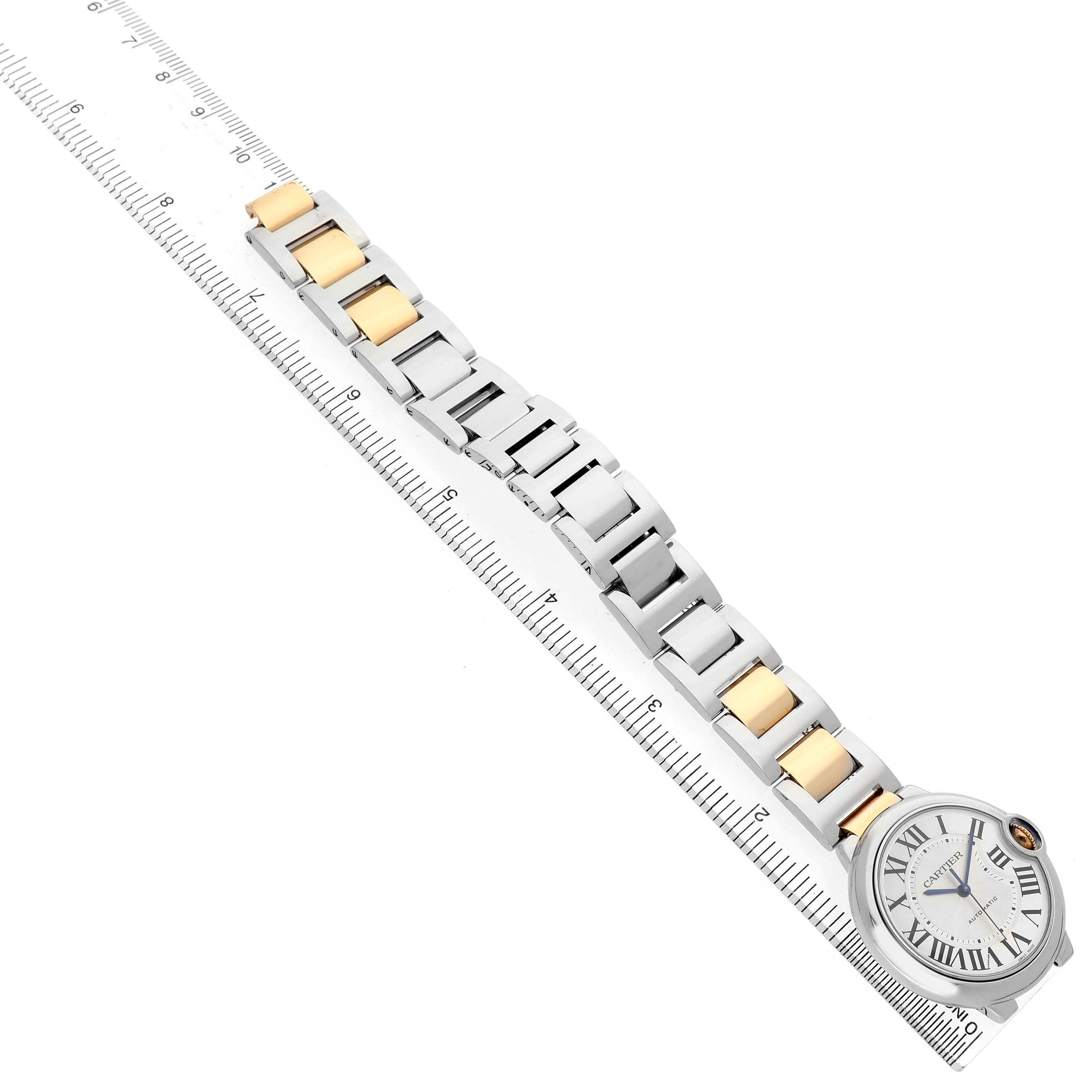The image shows a Cartier Ballon Bleu W6920047 Women's Steel and Gold (two tone) Silver Dial watch from above, displaying the face and full two-tone bracelet alongside a ruler for scale.