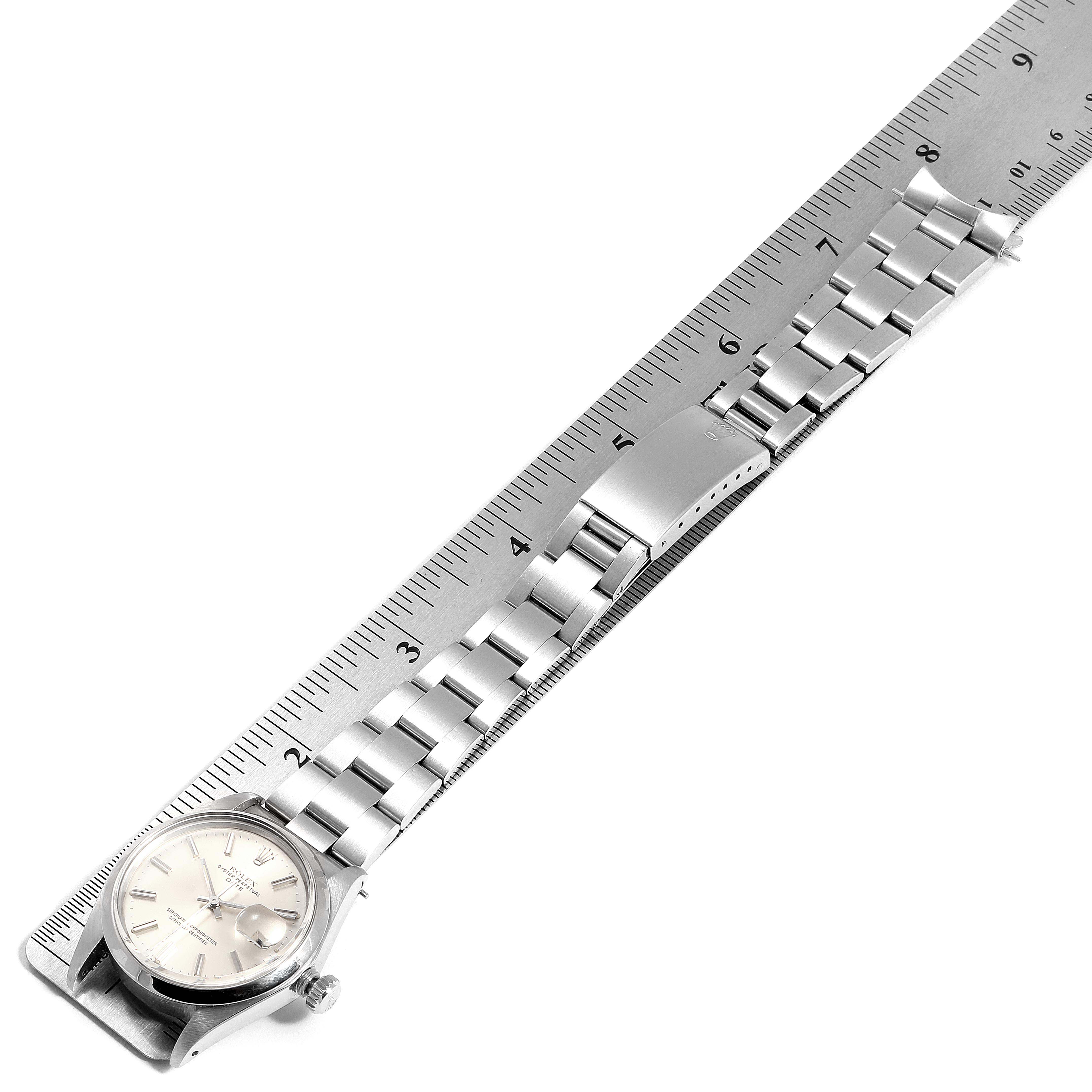 The Rolex Date 1500 Men's Stainless Steel Silver Dial 1500 Men's Stainless Steel Silver Dial watch is shown from a top-down angle, displaying the face, bracelet, and clasp, alongside a ruler for scale.