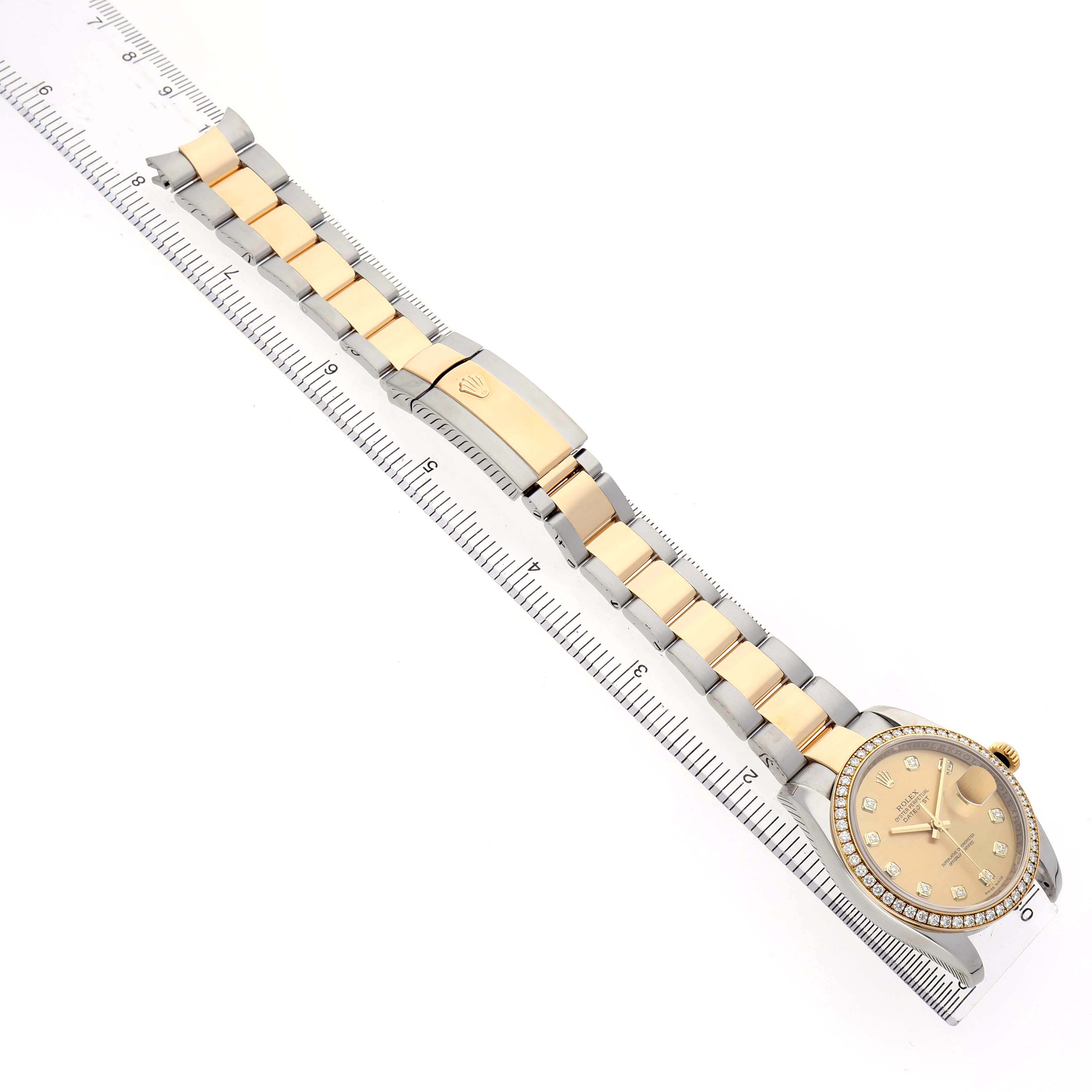 The image shows a Rolex Datejust 116243 Men's Steel and Gold (two tone) Champagne Dial watch from an angled top-down view, displaying the entire bracelet and face alongside a ruler.