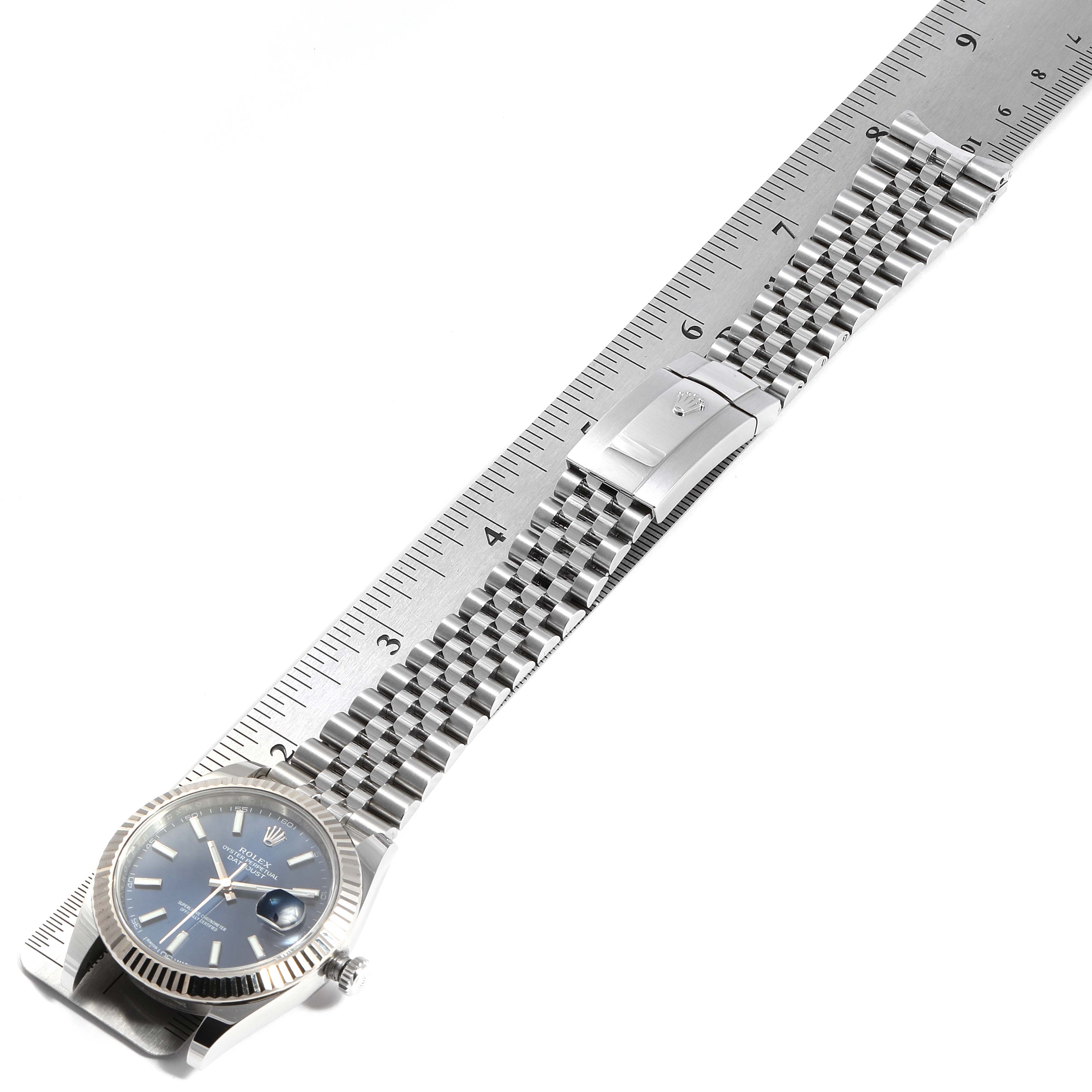 The Rolex Datejust 41 126334 Men
s Stainless Steel Blue Dial 126334 Men
s Stainless Steel Blue Dial watch is shown from an overhead angle displaying the face, bezel, bracelet, and clasp, next to a ruler.