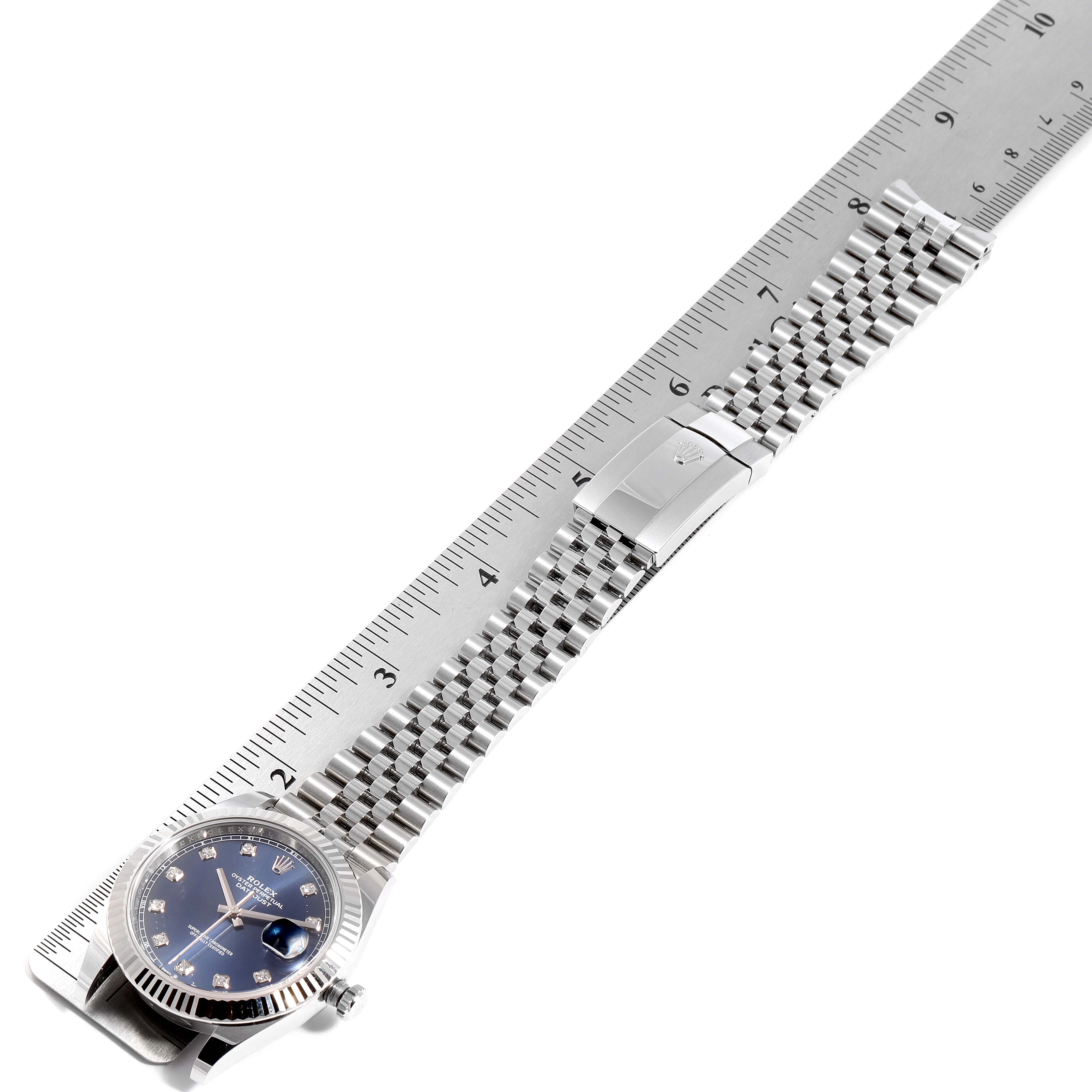 The image shows a top-down view of the Rolex Datejust 41 126334 Men
s Stainless Steel Blue Dial 126334 Men
s Stainless Steel Blue Dial watch, displaying its face, bracelet, and clasp next to a ruler for scale.
