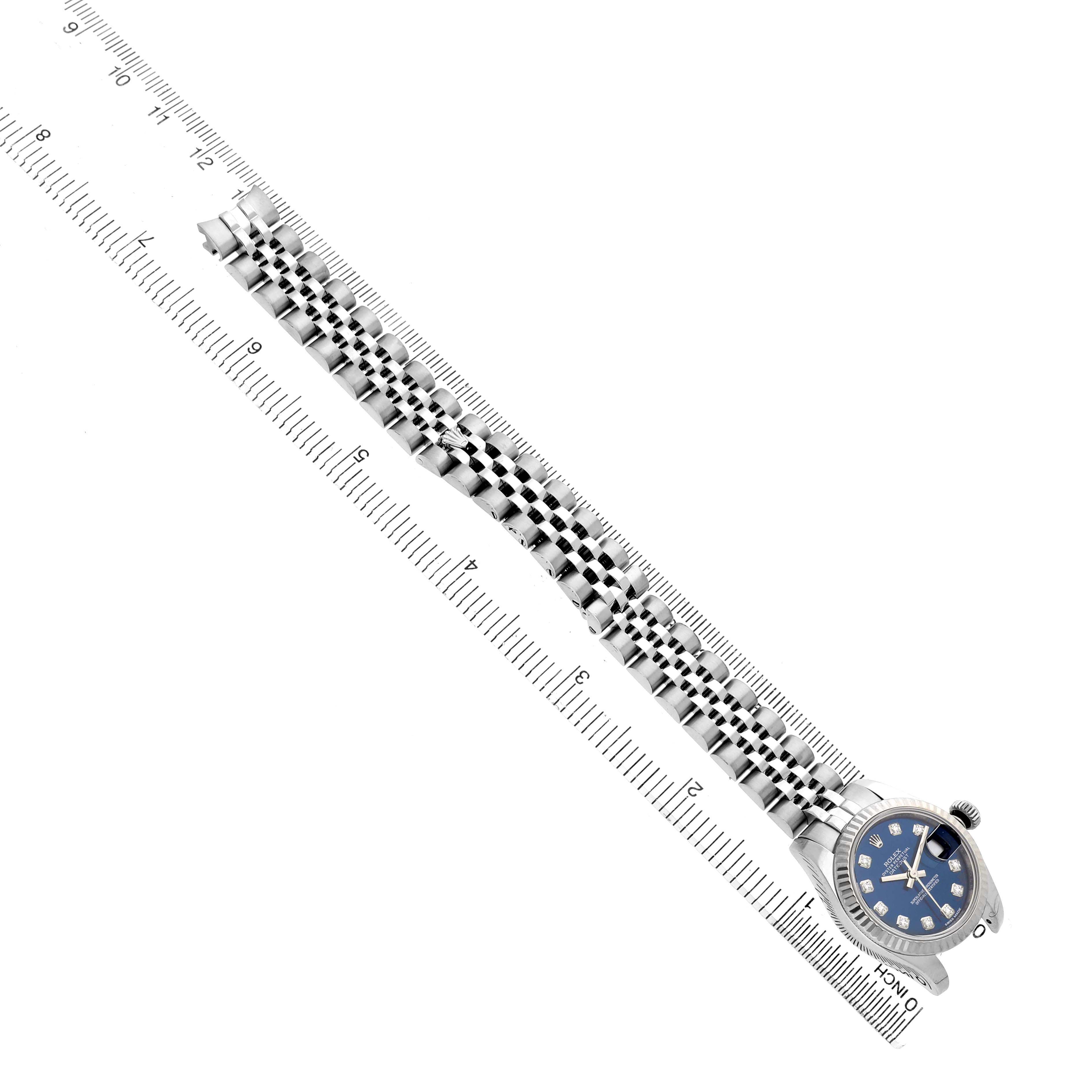 The Rolex Datejust 179174 Women's Stainless Steel Blue Dial watch is shown from a top angle alongside a ruler, displaying its full bracelet and watch face.