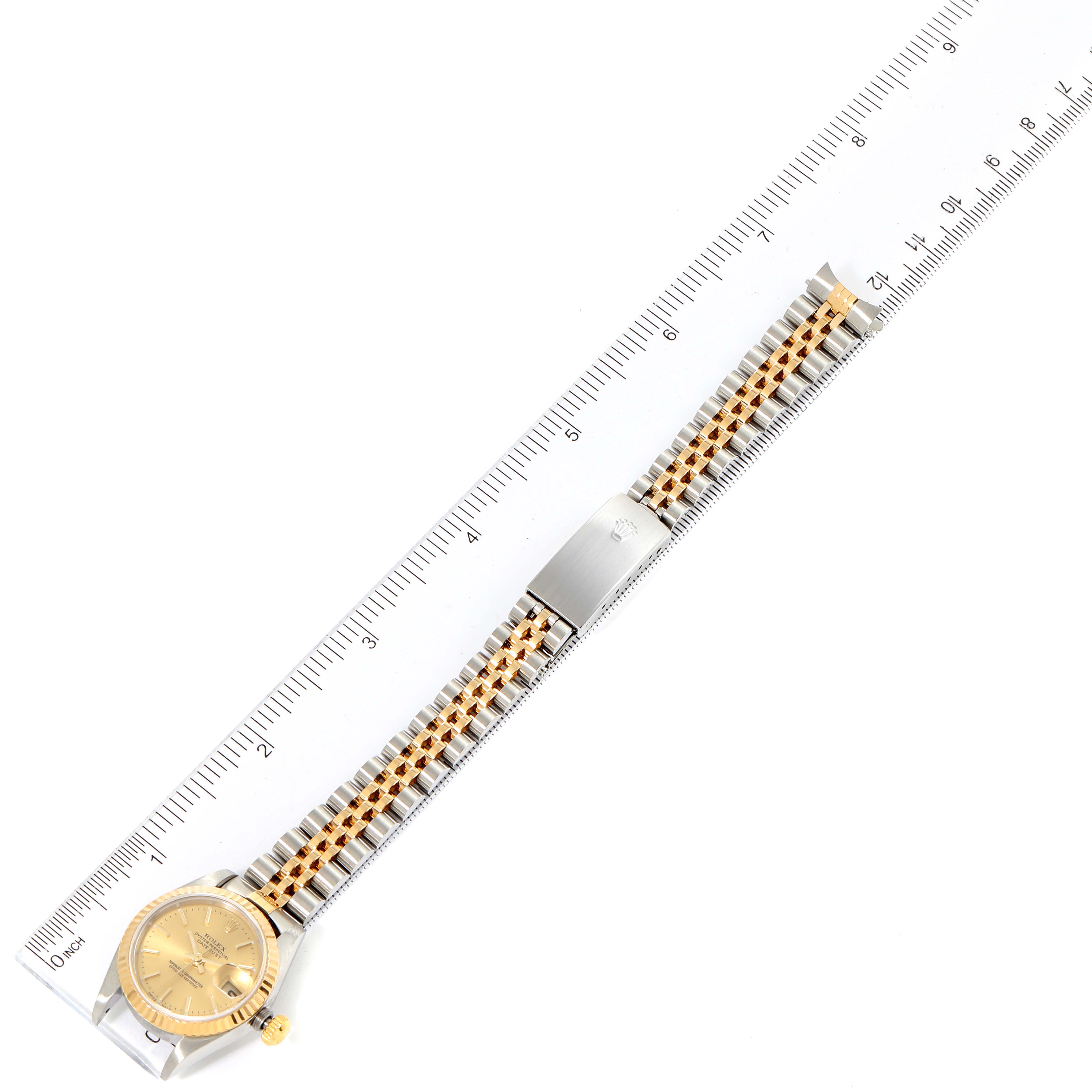 The Rolex Datejust 79173 Women's Steel and Gold (two tone) Champagne Dial 79173 Women's Steel and Gold (two tone) Champagne Dial watch is shown from a top view, including the face, bezel, and entire bracelet alongside a ruler for scale.