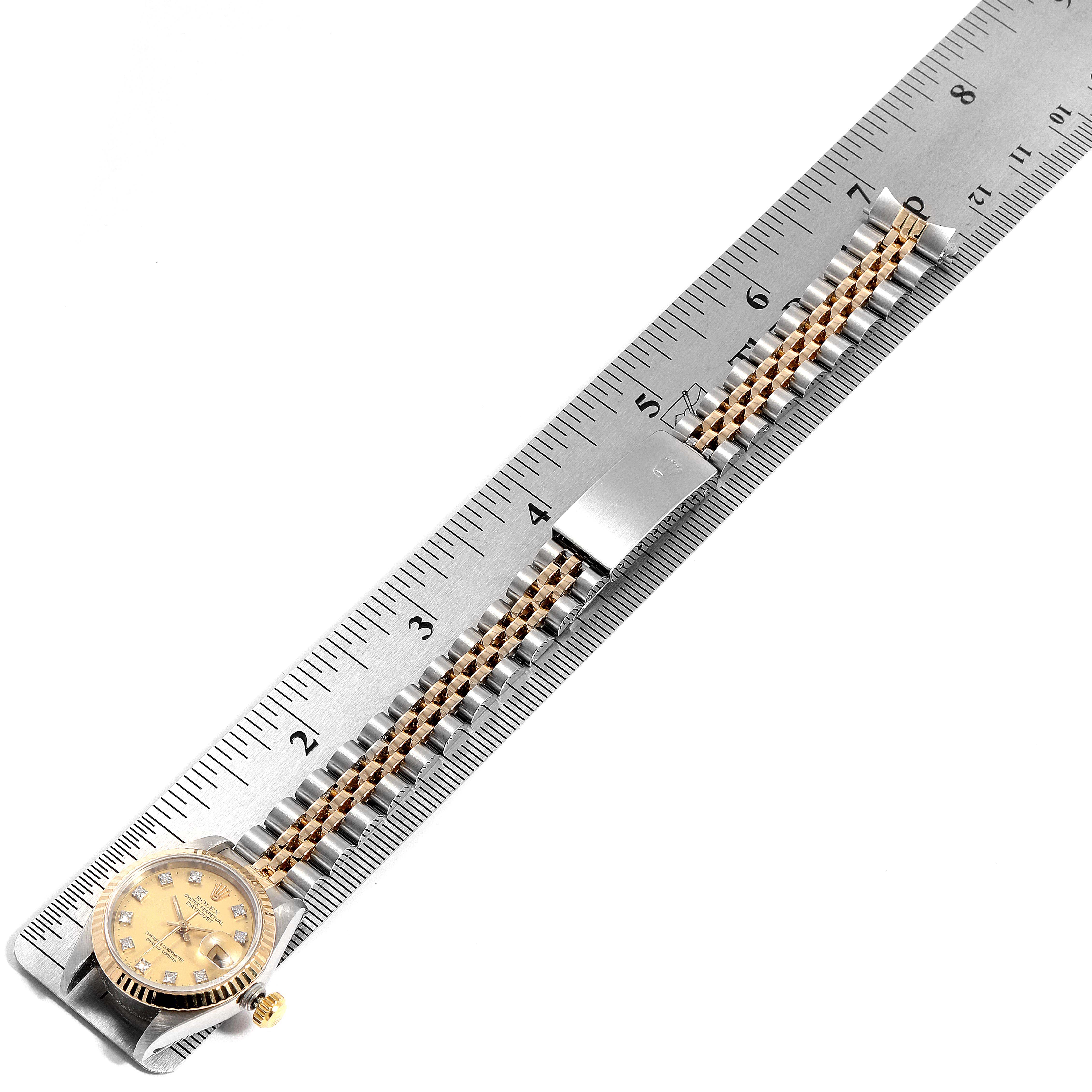 This image shows a top view of a Rolex Datejust 69173 Women
s Steel and Gold (two tone) Champagne Dial 69173 Women
s Steel and Gold (two tone) Champagne Dial, focusing on the face and bracelet aligned along a metal ruler.