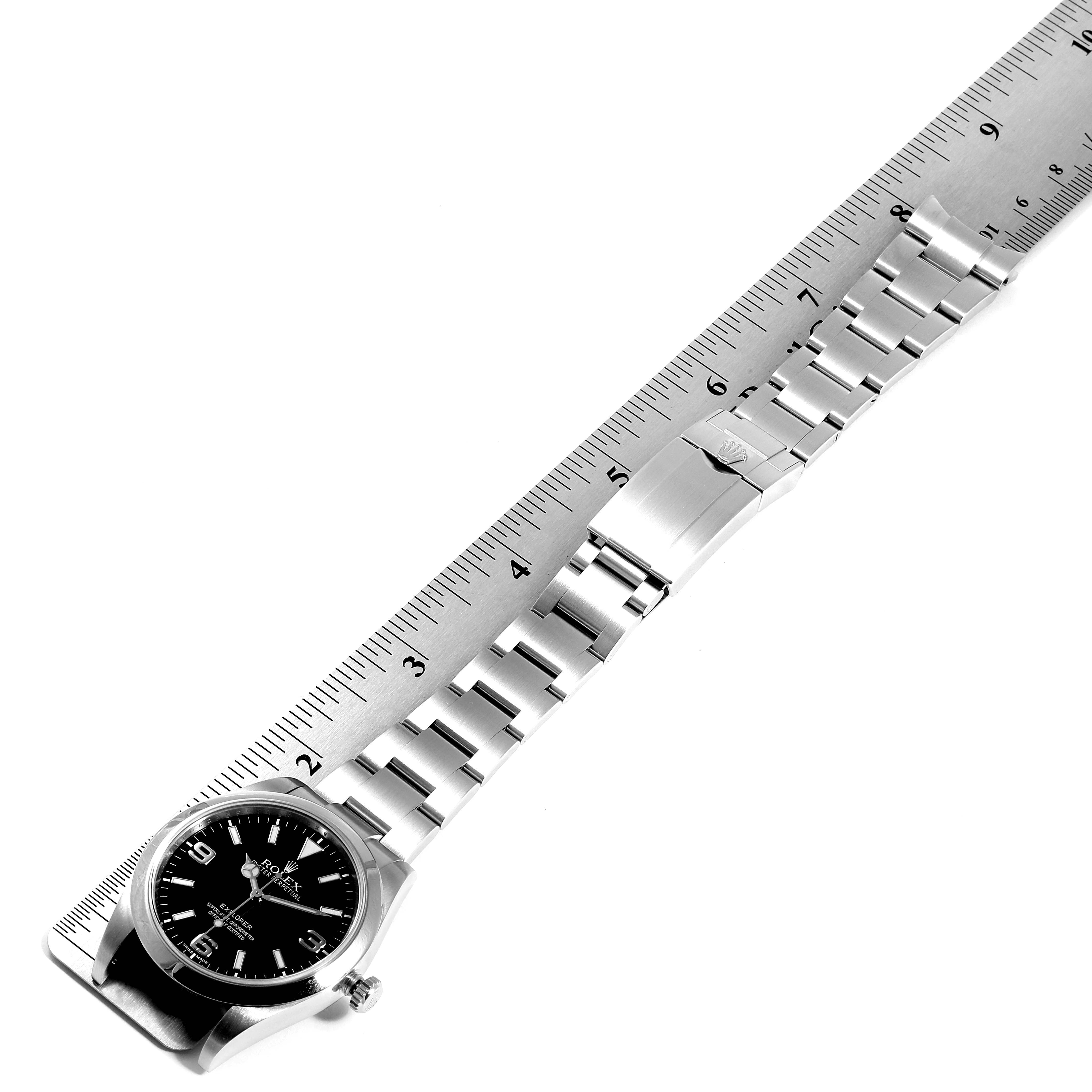 The image shows a top-down view of a Rolex Explorer 214270 Men
s Stainless Steel Black Dial 214270 Men
s Stainless Steel Black Dial watch laid alongside a ruler.