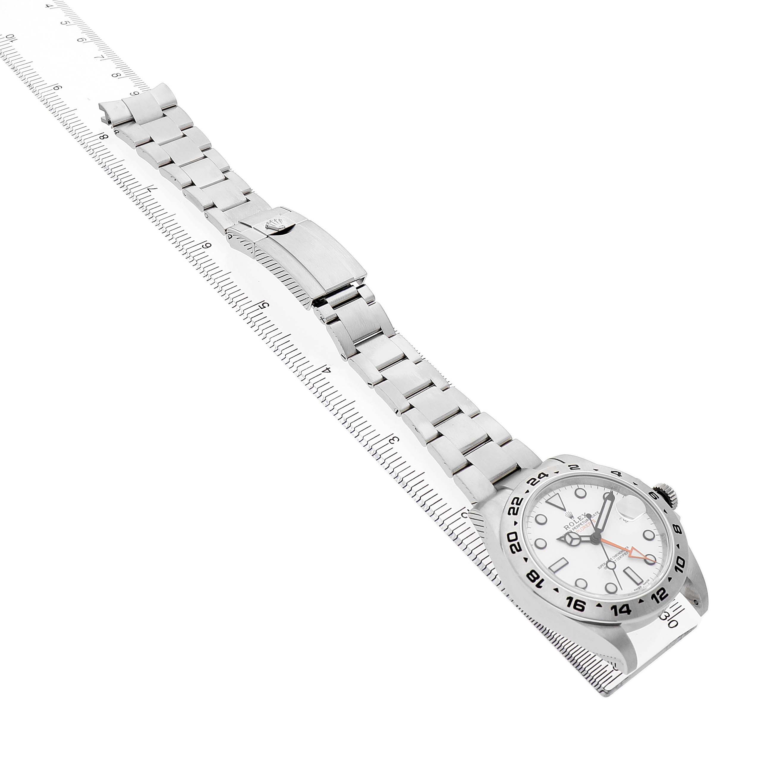 The Rolex Explorer 216570 Men's Stainless Steel White Dial watch is shown at an angled view, featuring the full bracelet, clasp, and face with a ruler alongside.