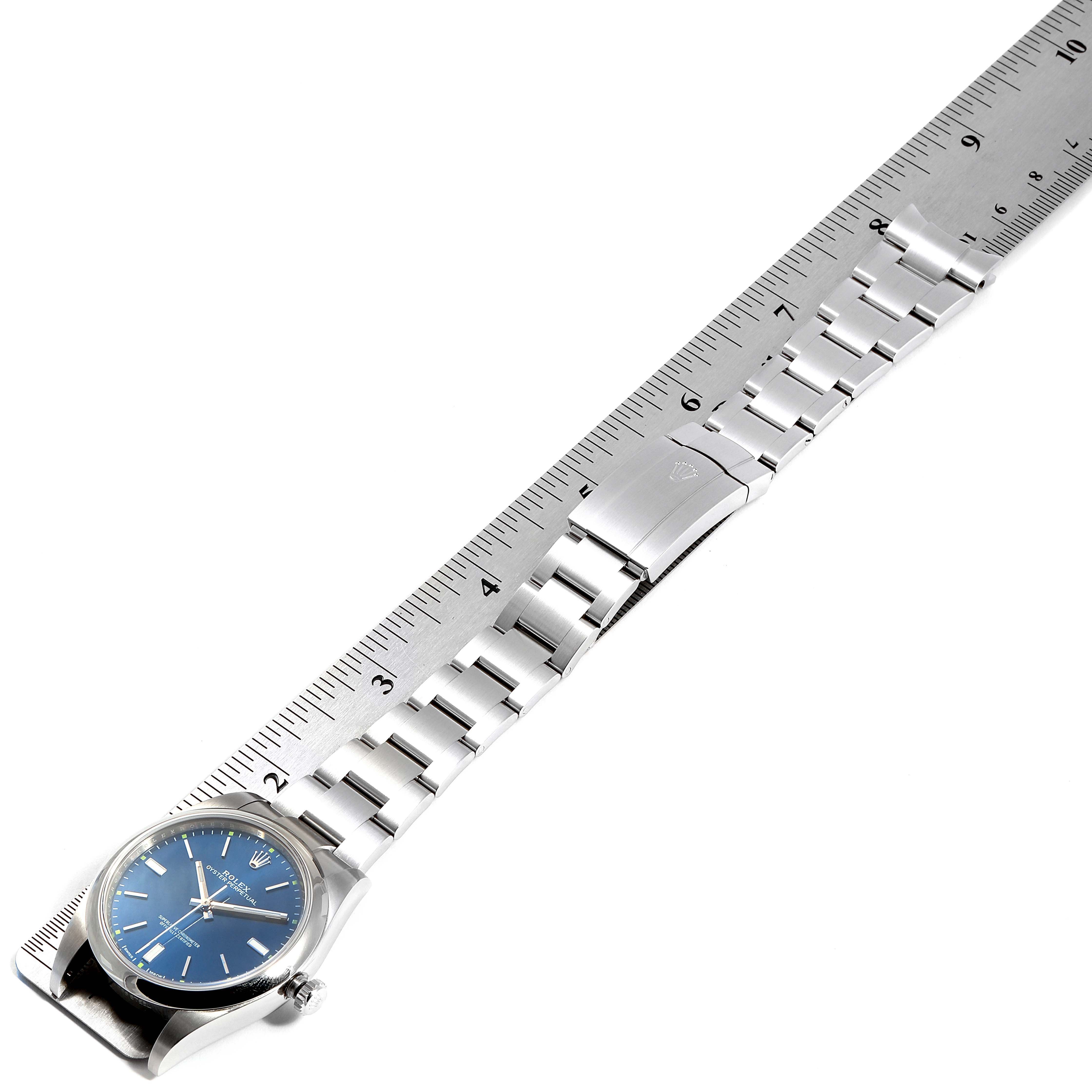 The Rolex Oyster Perpetual 114300 Men's Stainless Steel Blue Dial 114300 Men's Stainless Steel Blue Dial watch is shown laid flat along a ruler, displaying the face, bracelet, and clasp.