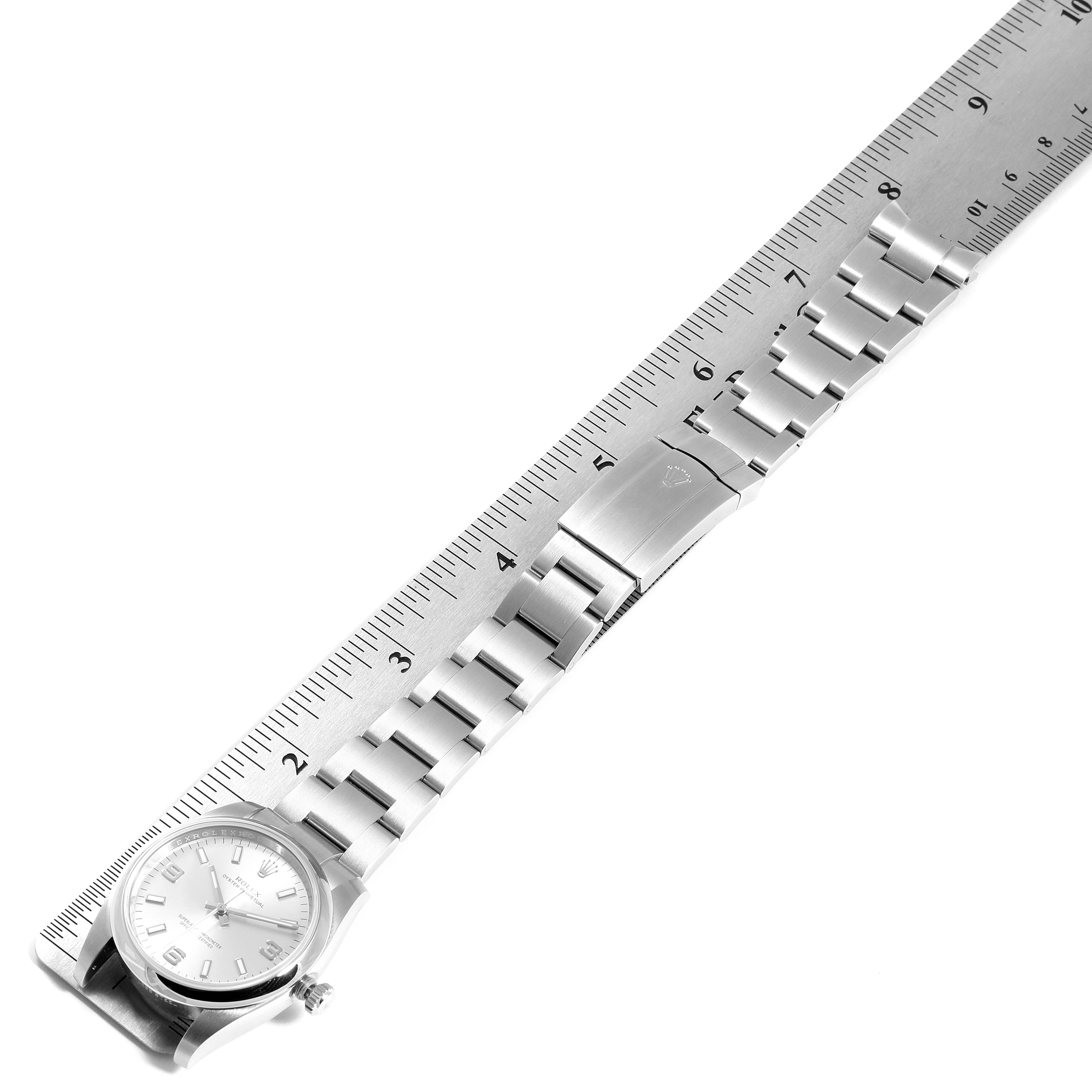 The image shows a top view of a Rolex Oyster Perpetual 114200 Men's Stainless Steel Silver Dial 114200 Men's Stainless Steel Silver Dial watch with its stainless steel band aligned next to a ruler.