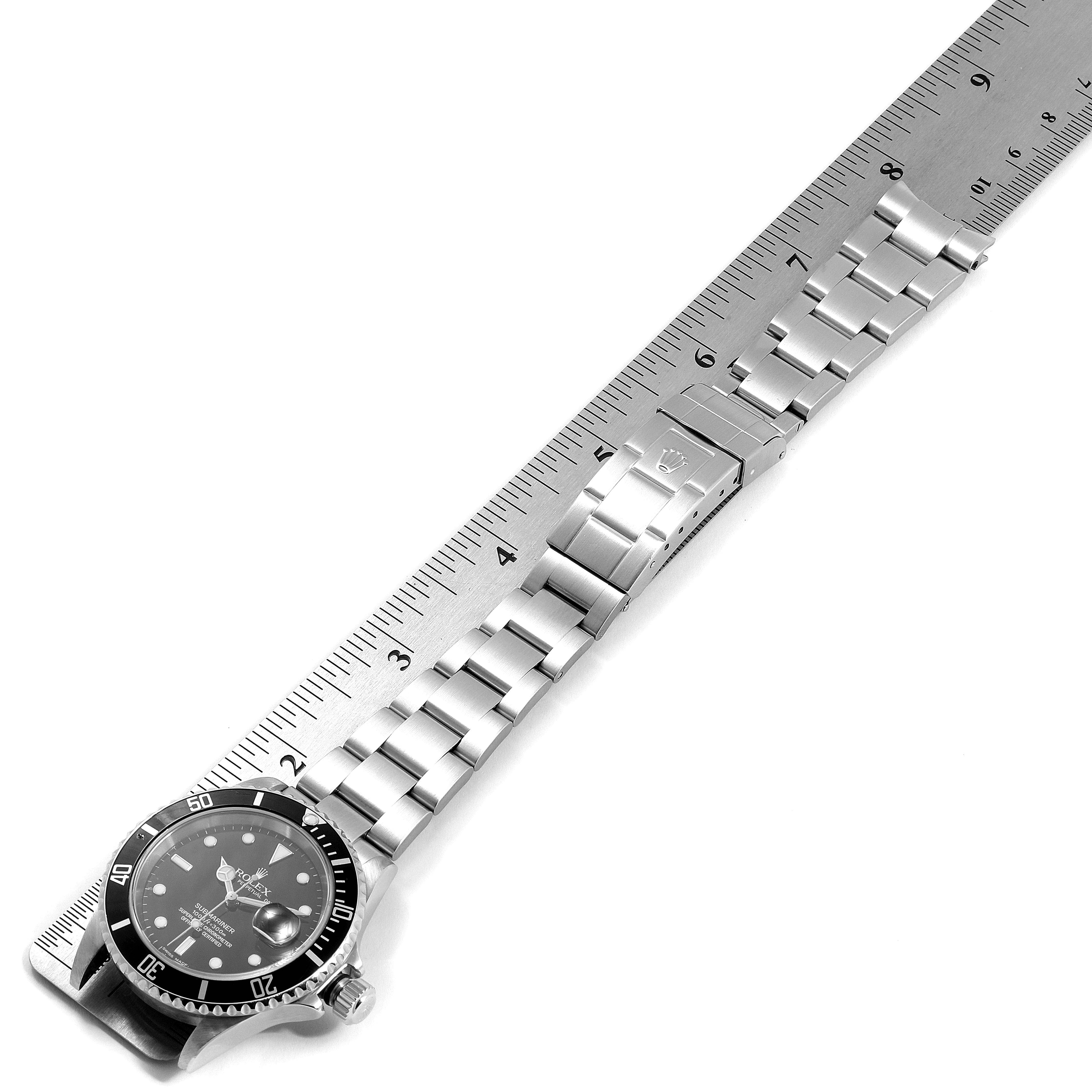 The image shows a top-down view of a Rolex Submariner 16610 Men
s Stainless Steel Black Dial 16610 Men
s Stainless Steel Black Dial watch with its band fully extended next to a ruler.