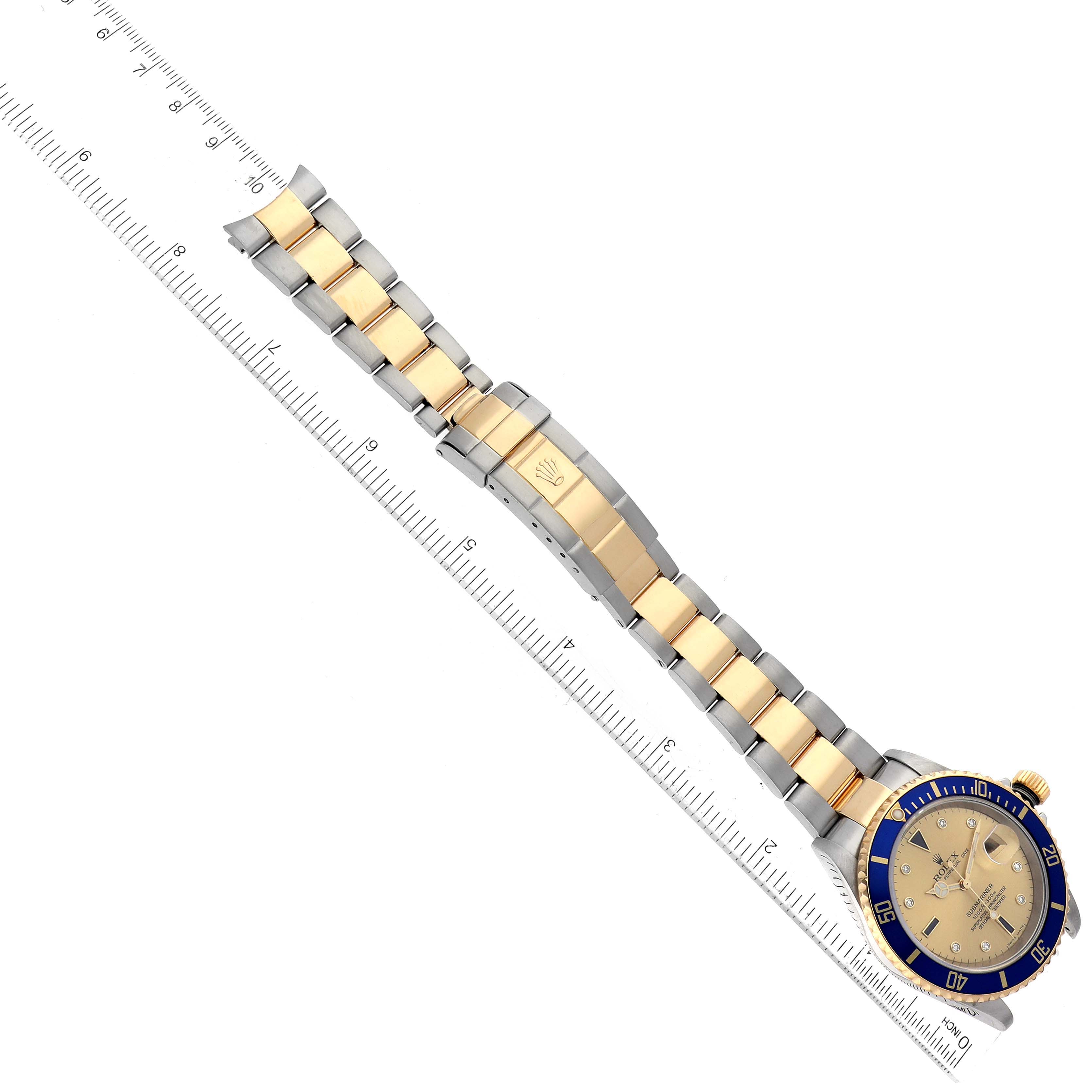 The image shows a top view of a Rolex Submariner 16613 Men's Steel and Gold (two tone) Champagne Dial 16613 Men's Steel and Gold (two tone) Champagne Dial watch with a gold and silver bracelet next to a ruler.