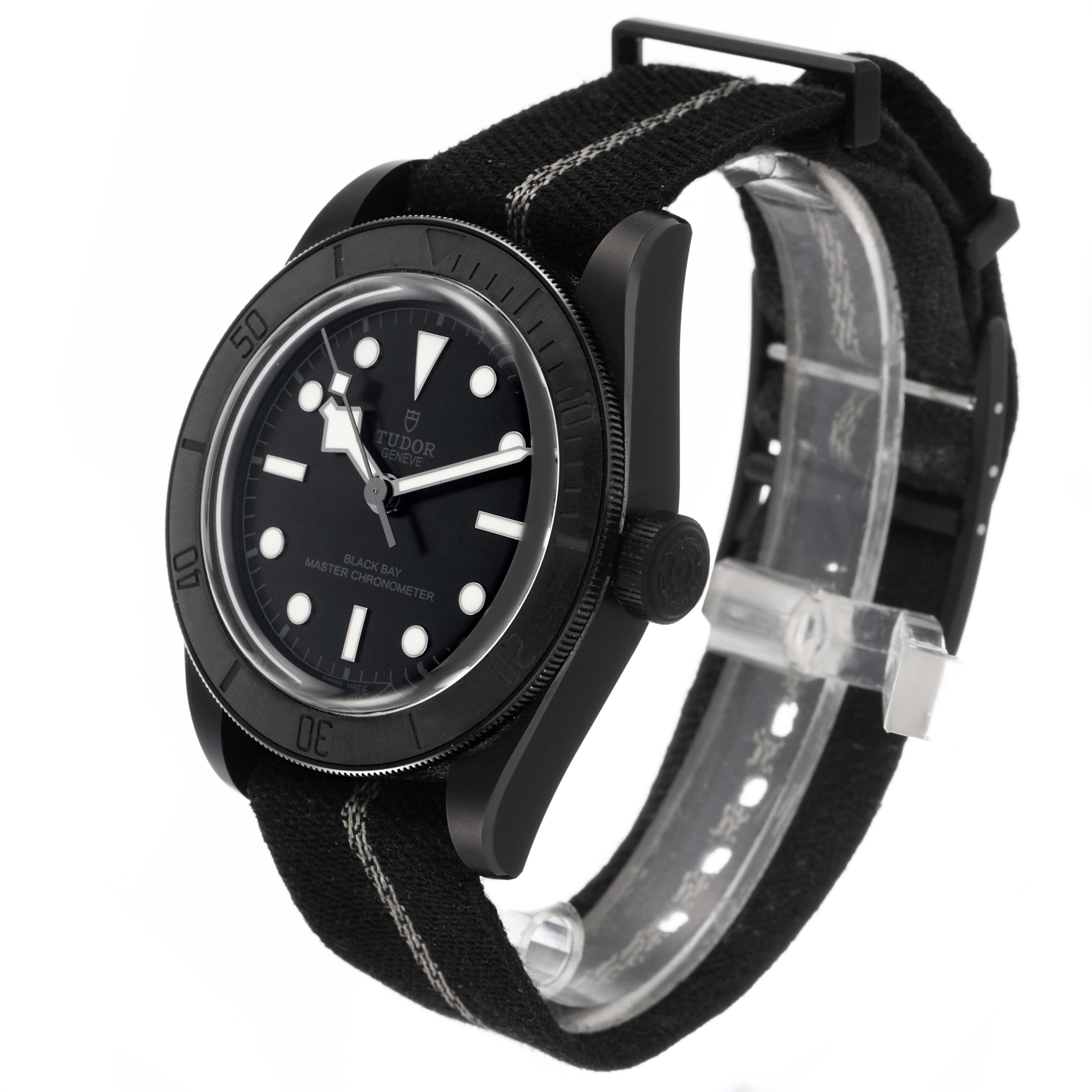 The Tudor Heritage Black Bay M79210CNU Men's Ceramic Black Dial watch is shown at a three-quarter angle, highlighting the dial, bezel, and fabric strap.