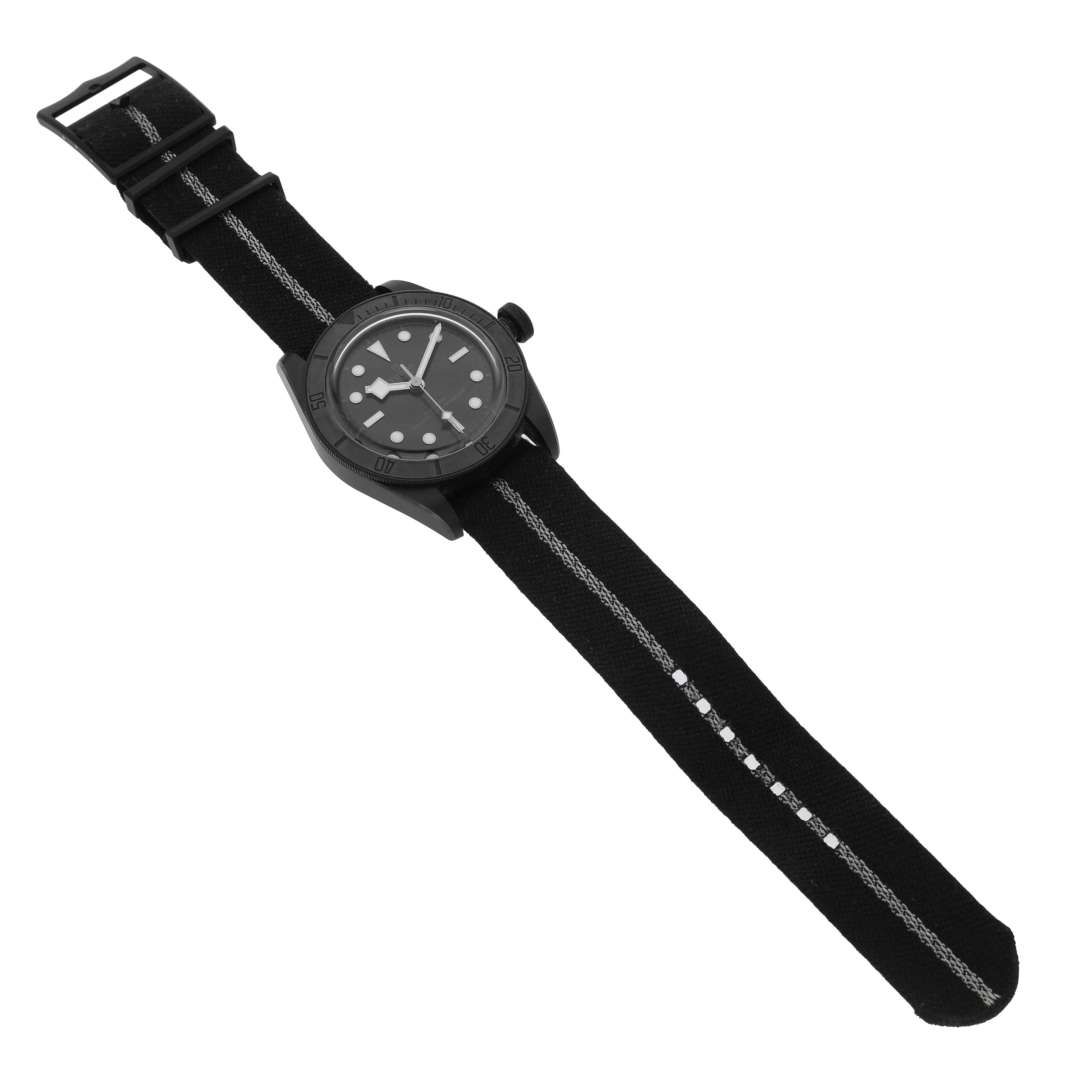 The Tudor Heritage Black Bay M79210CNU Men's Ceramic Black Dial watch is shown from a top-down angle, featuring a dark dial and a fabric strap.