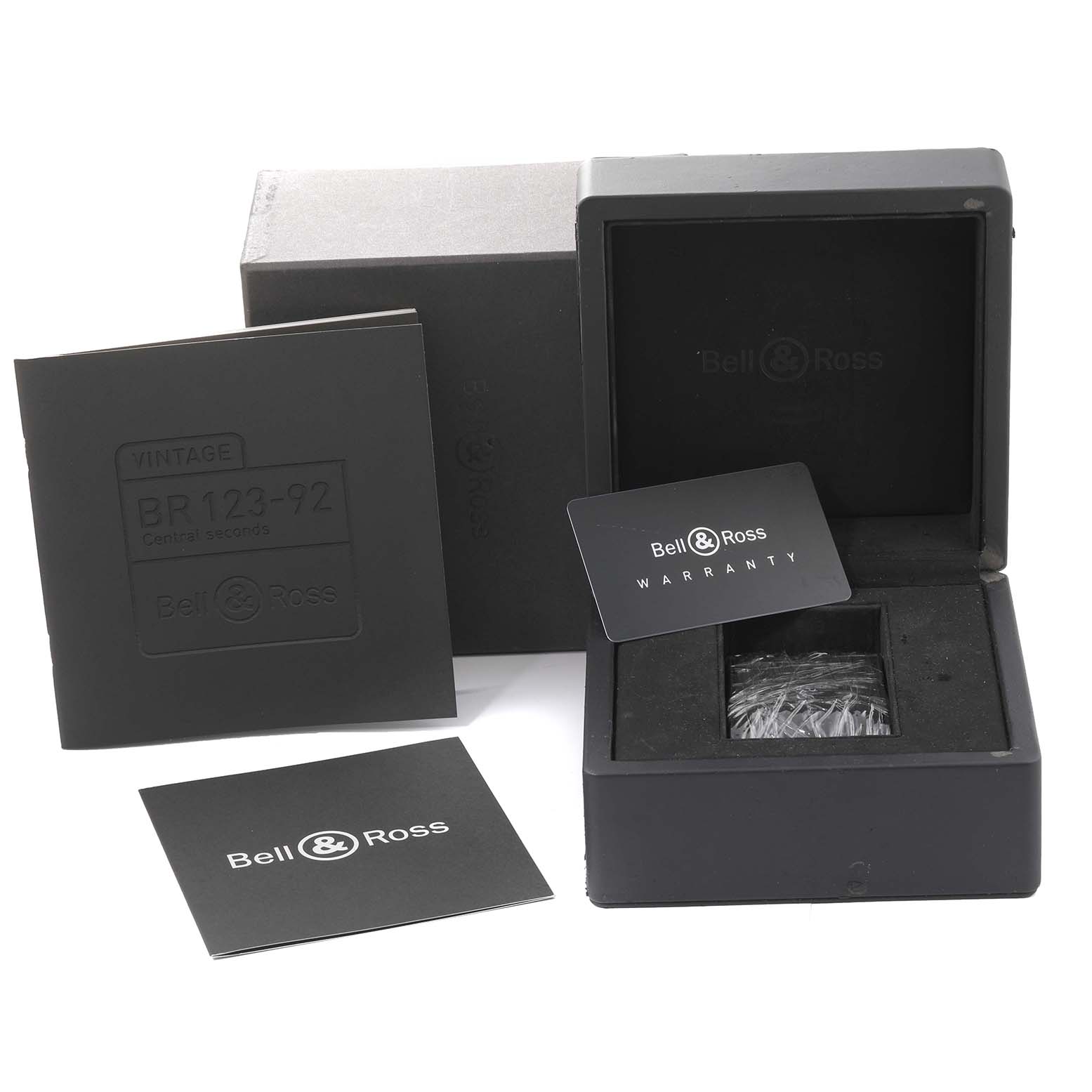 The image shows the box, a warranty card, and documents for the Bell 
Ross Heritage BR 123-92-SP Men
s Stainless Steel Black Dial BR 123-92-SP Men
s Stainless Steel Black Dial model watch.