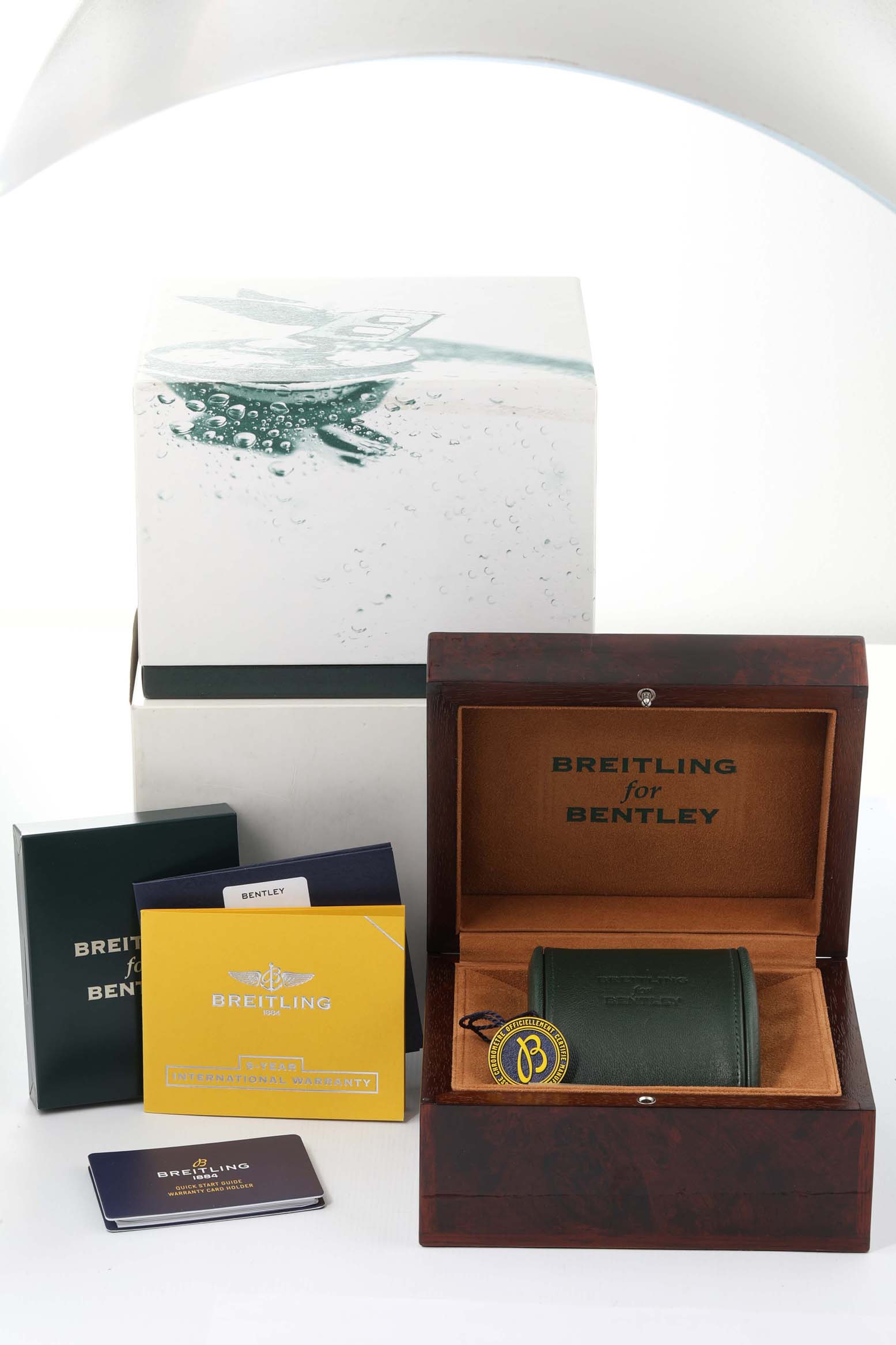 The image shows packaging and accessories for the Bentley model by Breitling, including boxes, booklets, and a watch case.