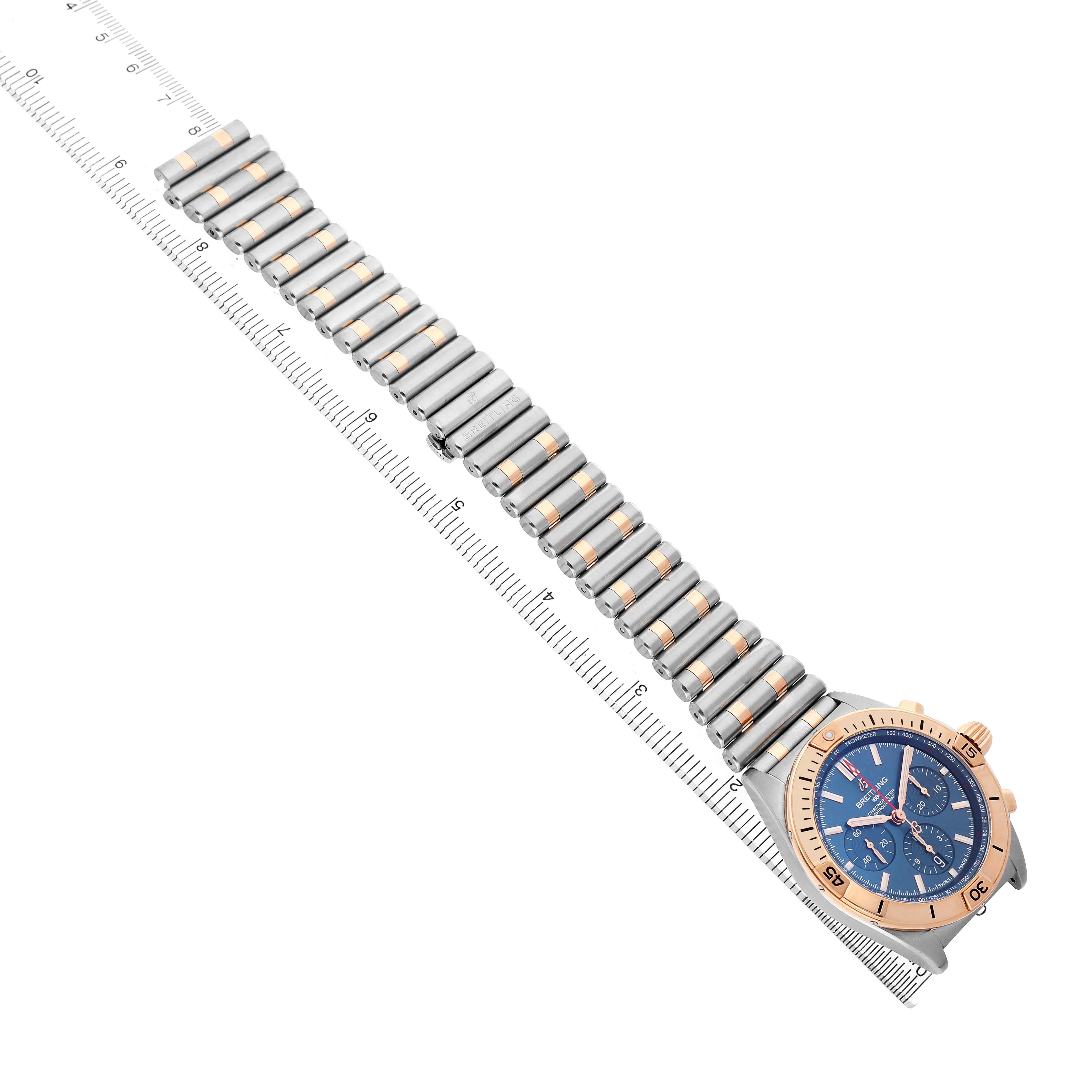 The Breitling Chronomat UB0134101C1U1 Men's Stainless Steel Blue Dial watch is shown from an angle highlighting the bracelet and face, laid alongside a ruler for scale.