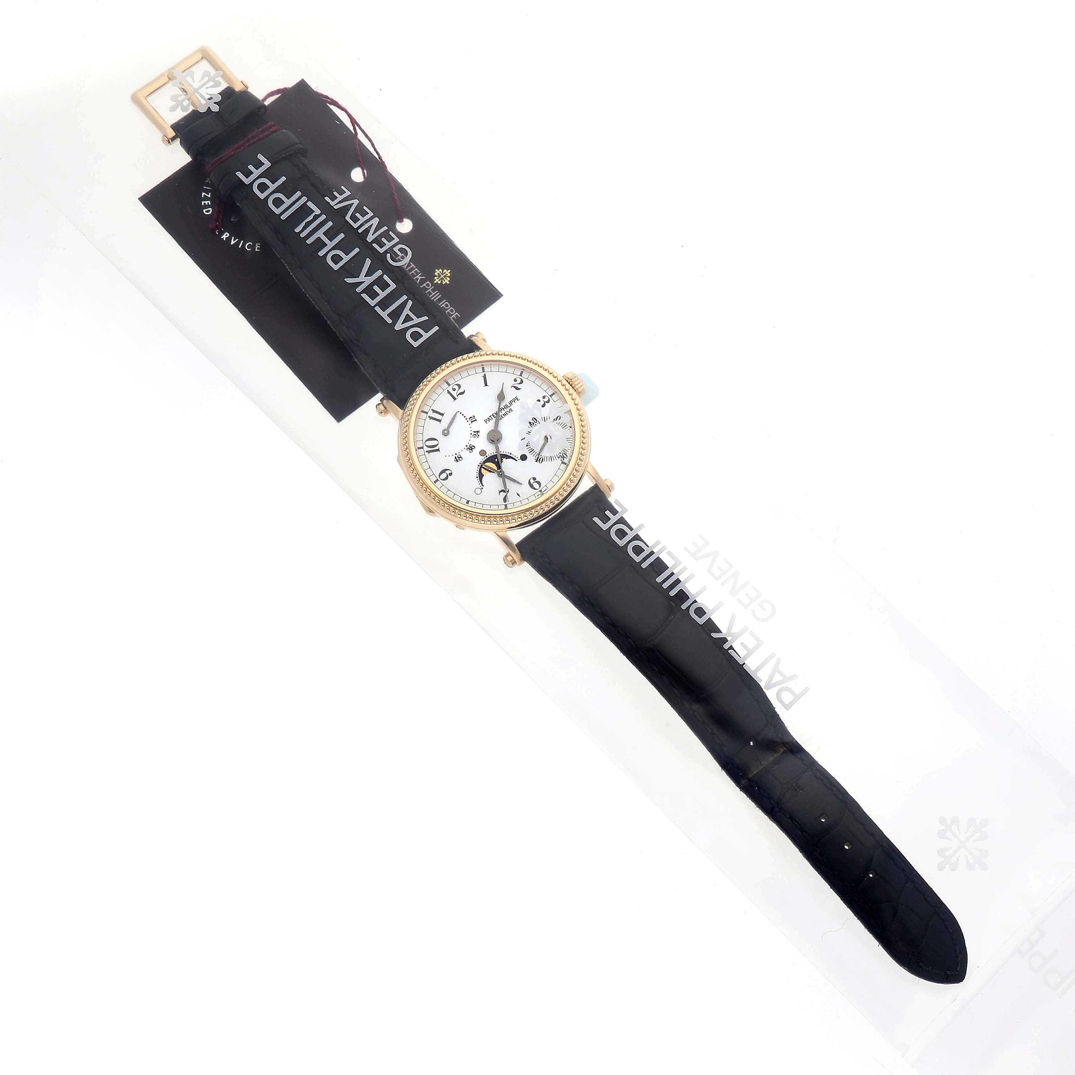 The Patek Philippe Calatrava 5015J-001 Men's Yellow Gold White Dial watch is shown from a top-down angle, displaying the face, bezel, and strap with a visible tag.