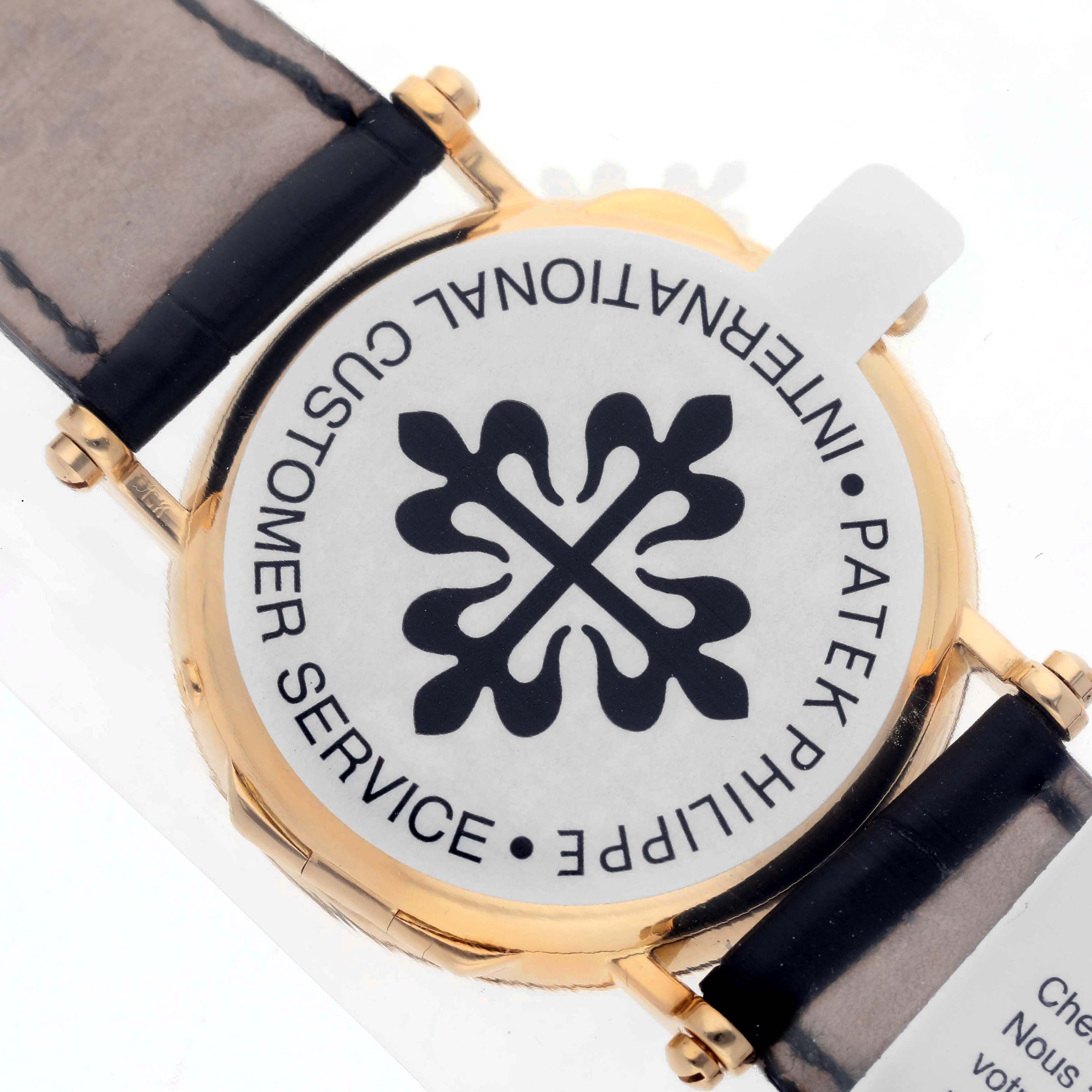 The image shows the back of a Patek Philippe Calatrava 5015J-001 Men's Yellow Gold White Dial watch, highlighting the logo and strap attachments.