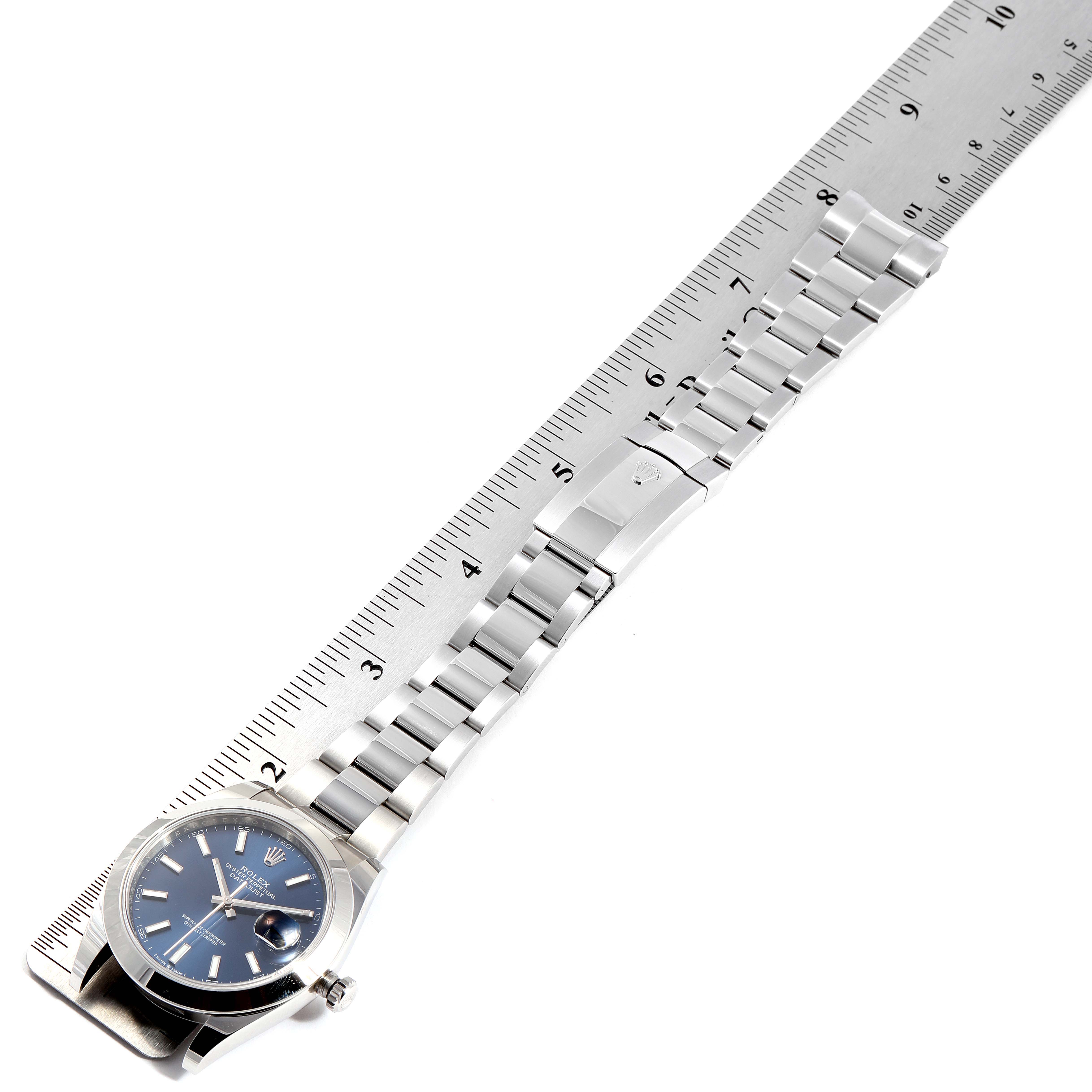 A Rolex Datejust 41 126300 Men
s Stainless Steel Blue Dial 126300 Men
s Stainless Steel Blue Dial watch is shown lying flat with its metal bracelet extended, alongside a ruler for size reference.