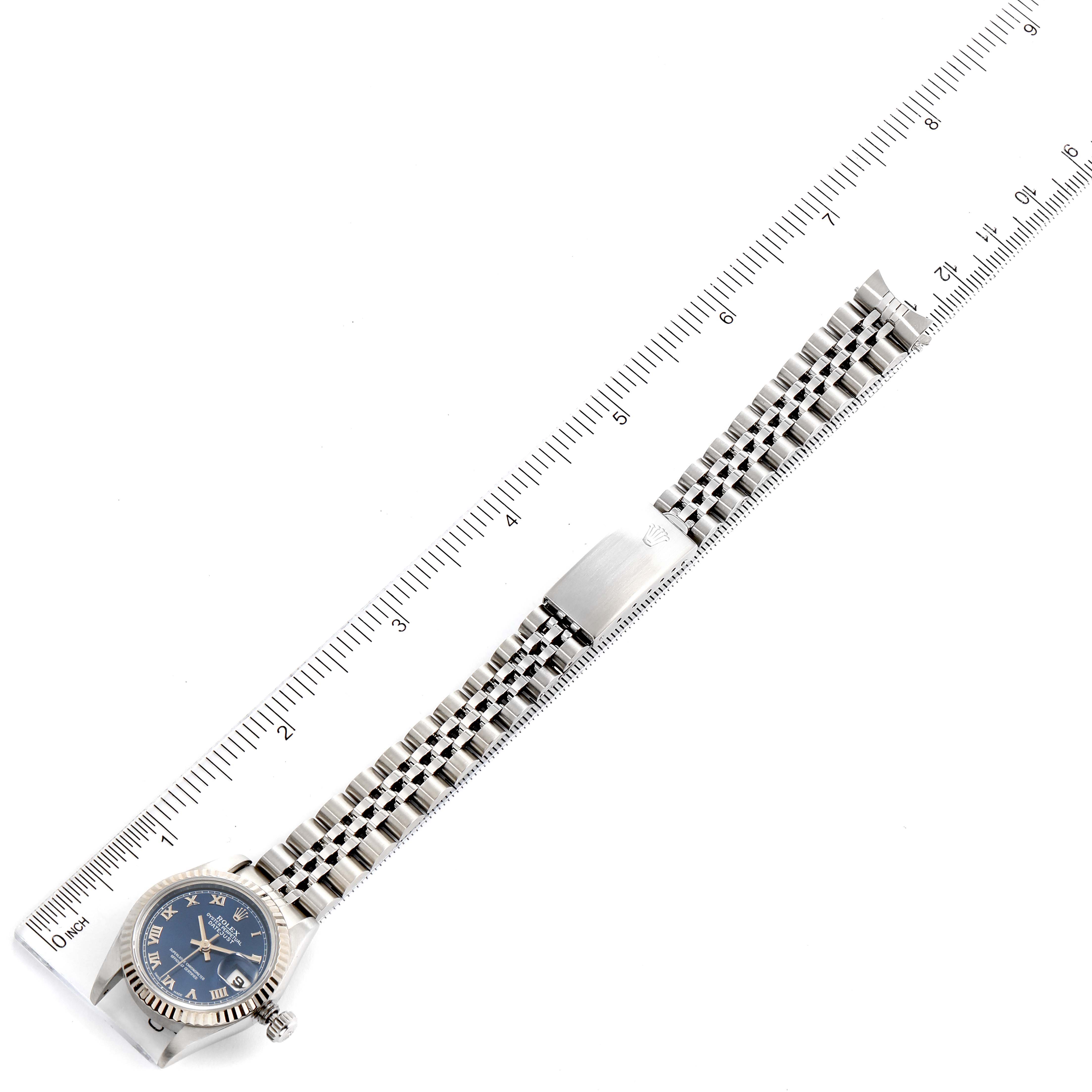 The image shows a Rolex Datejust 69174 Women
s Stainless Steel Blue Dial 69174 Women
s Stainless Steel Blue Dial watch, positioned diagonally with the face and full bracelet visible, beside a ruler for scale.