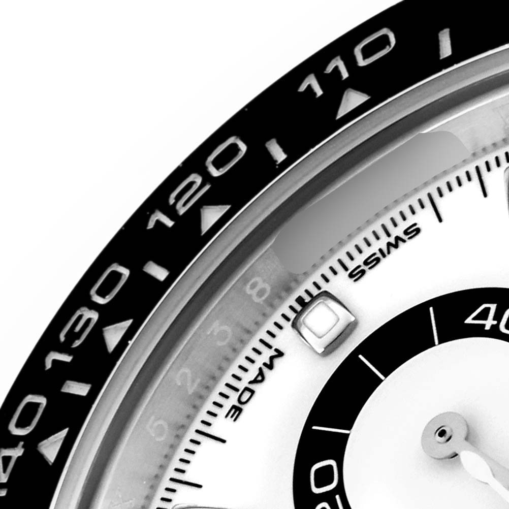 The image shows a close-up of the bezel and dial of a Rolex Daytona 116500 Men
s Stainless Steel White Dial, highlighting the tachymetric scale and part of the chrono register.
