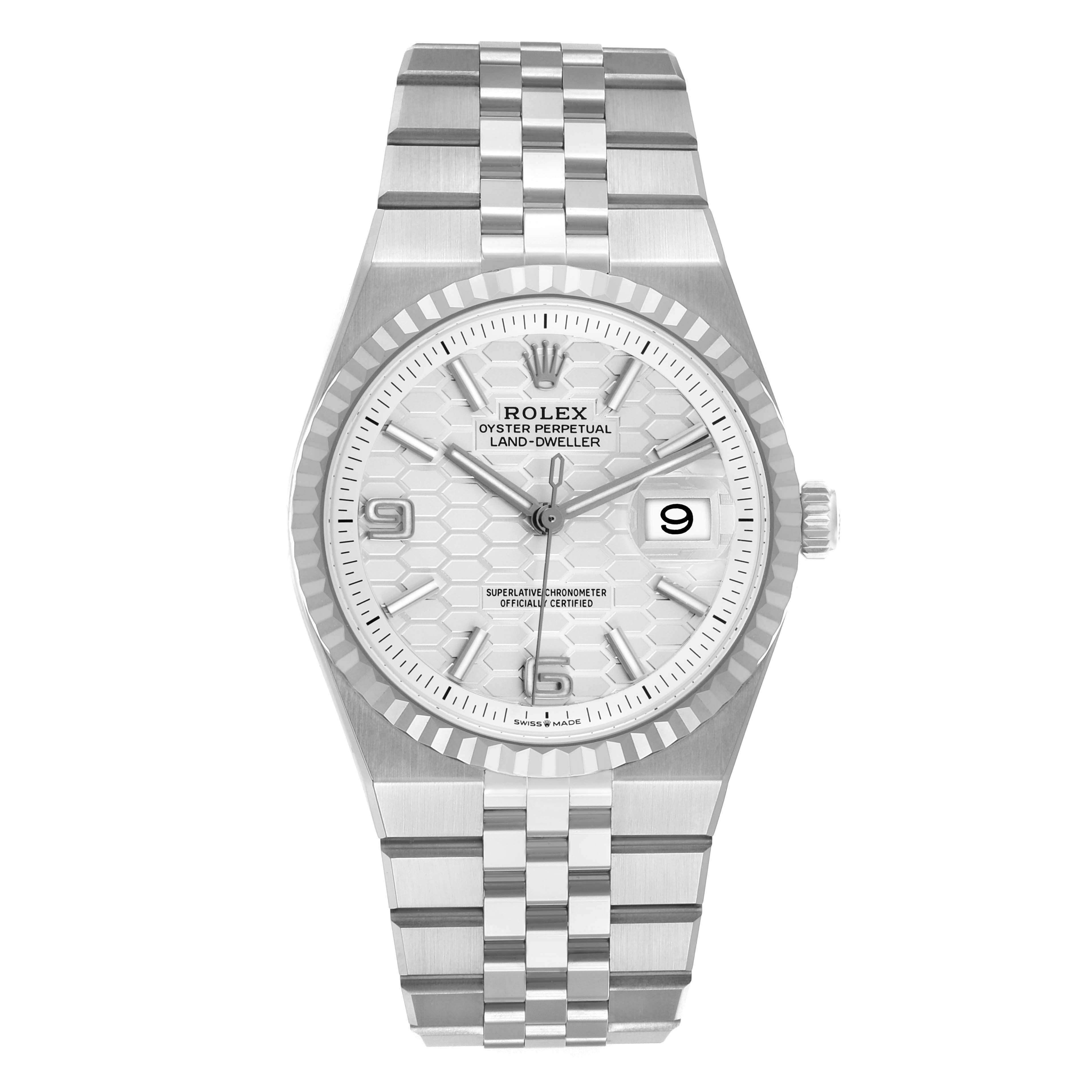 The Rolex Land-Dweller watch is shown from a top-down angle, displaying the face, bezel, and bracelet.