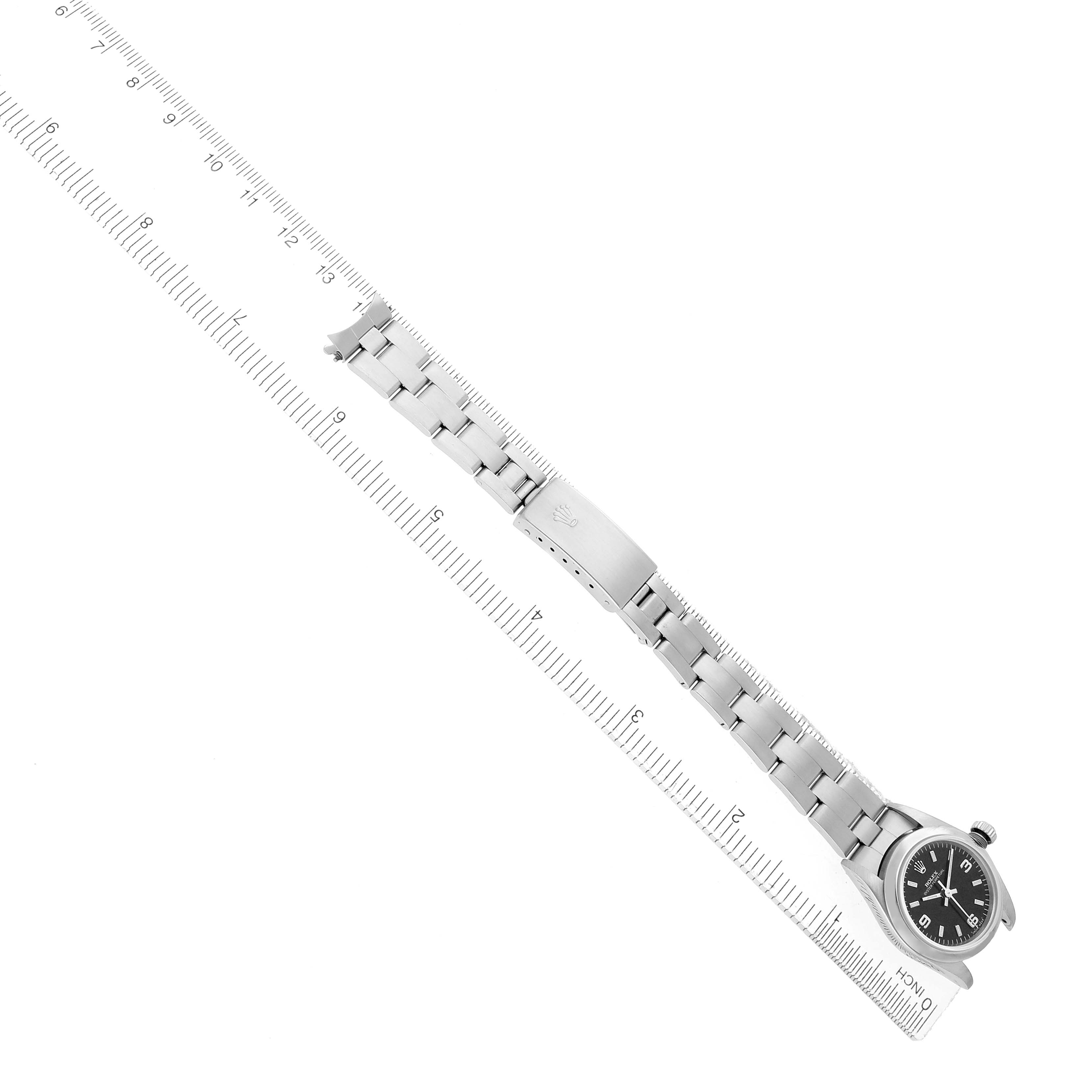 The Rolex Oyster Perpetual 76080 Women
s Stainless Steel Black Dial watch is shown flat from the top, displaying the dial, bracelet, and clasp alongside a ruler.