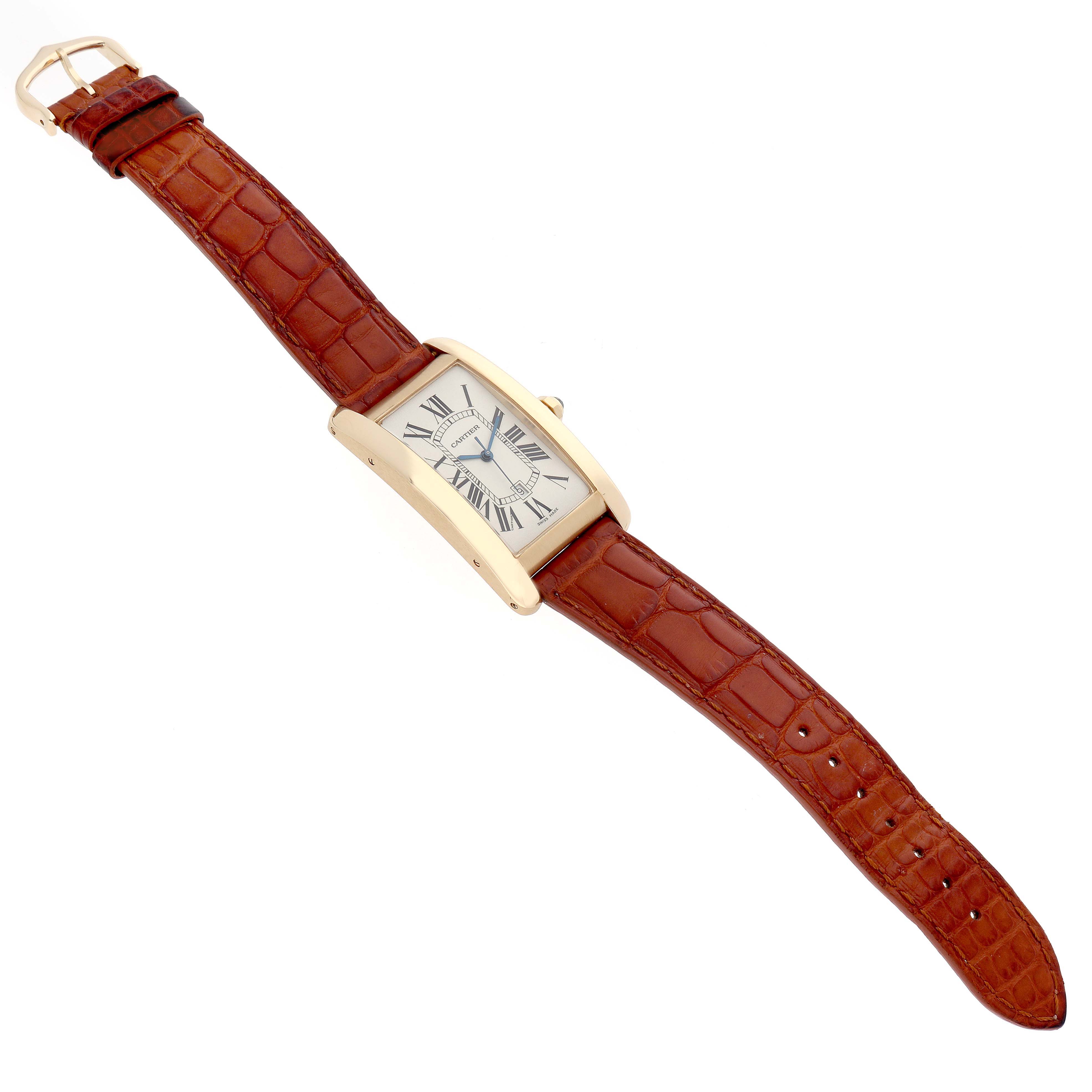 The Cartier Tank Américaine watch is shown at a slight diagonal angle, displaying its rectangular dial, gold case, and brown leather strap.