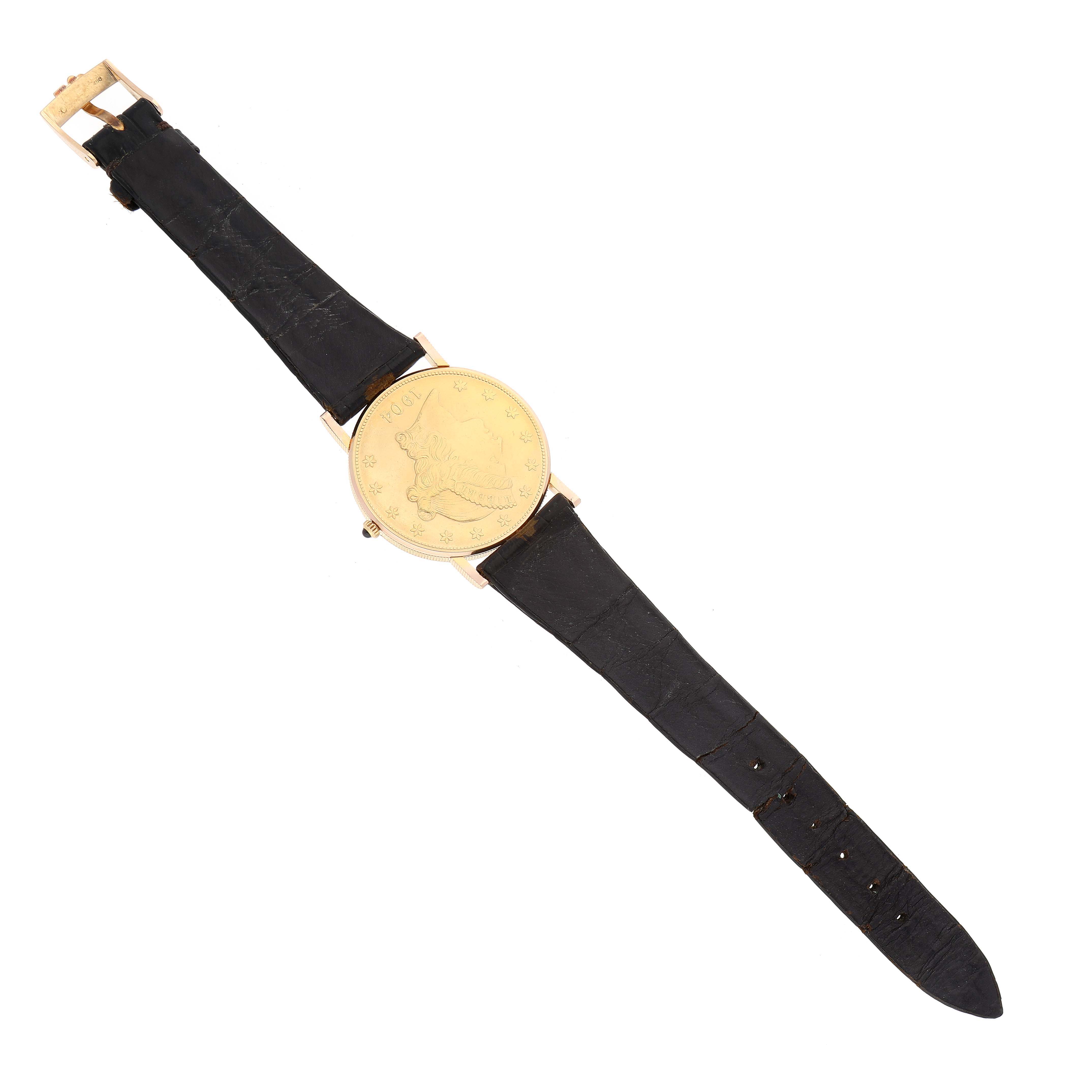 The image shows a full view of the Corum Coin Watch 1904 Men's Yellow Gold Champagne Dial 1904 Men's Yellow Gold Champagne Dial with a gold case and black leather strap laid flat.