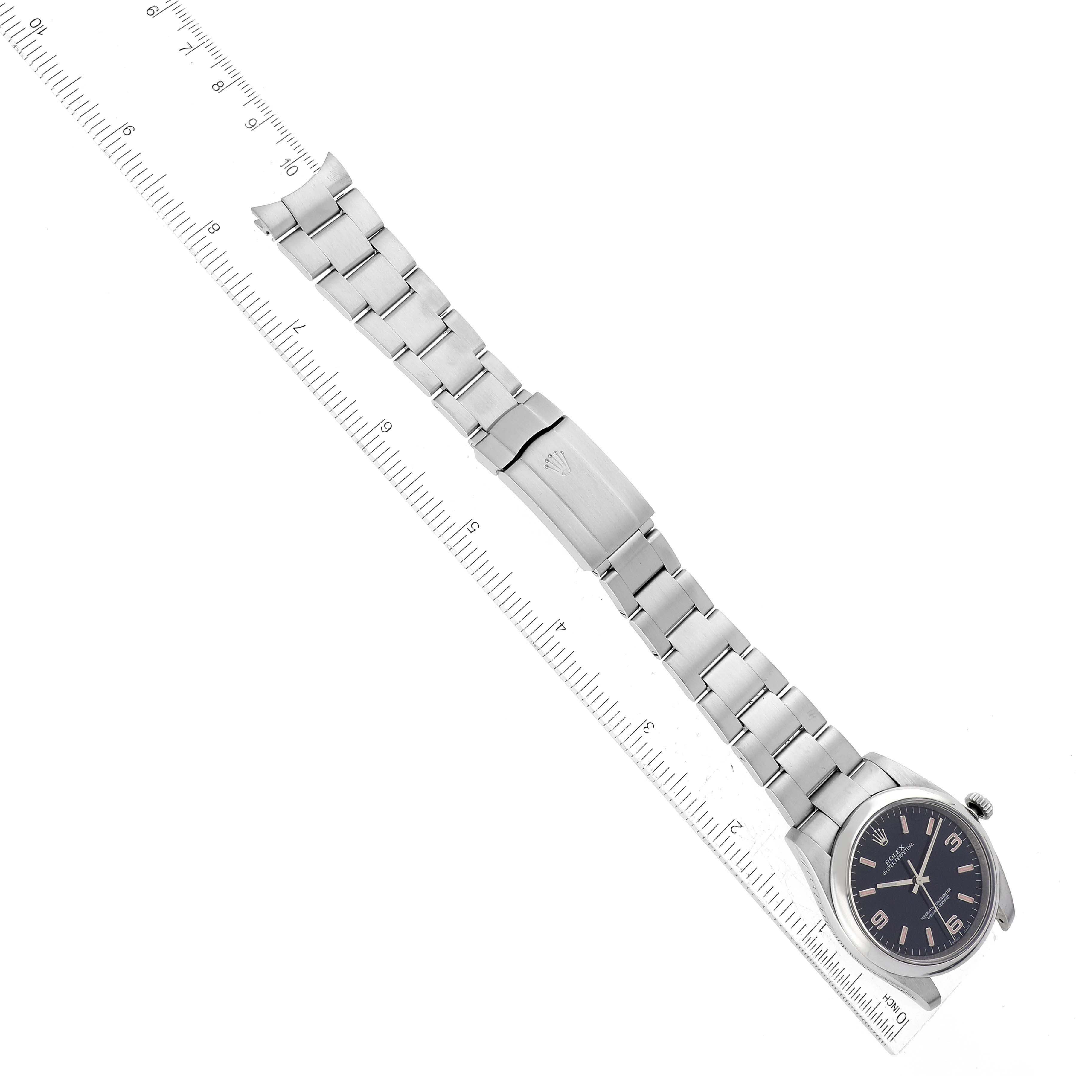 The image shows a top view of a Rolex Oyster Perpetual 116000 Men
s Stainless Steel Black Dial 116000 Men
s Stainless Steel Black Dial watch, displaying its face, bracelet, and clasp next to a ruler for scale.