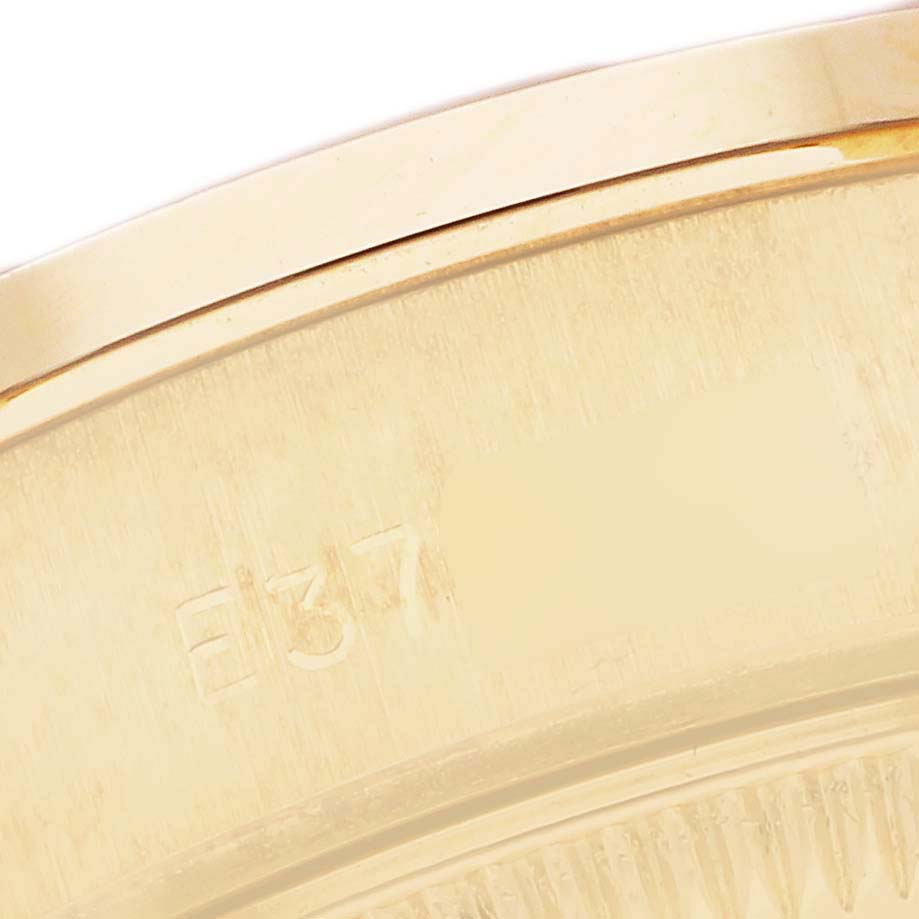 The image shows a close-up side angle of the Rolex President 69078 Women
s Yellow Gold Champagne Dial watch case, highlighting part of the engraved serial number.