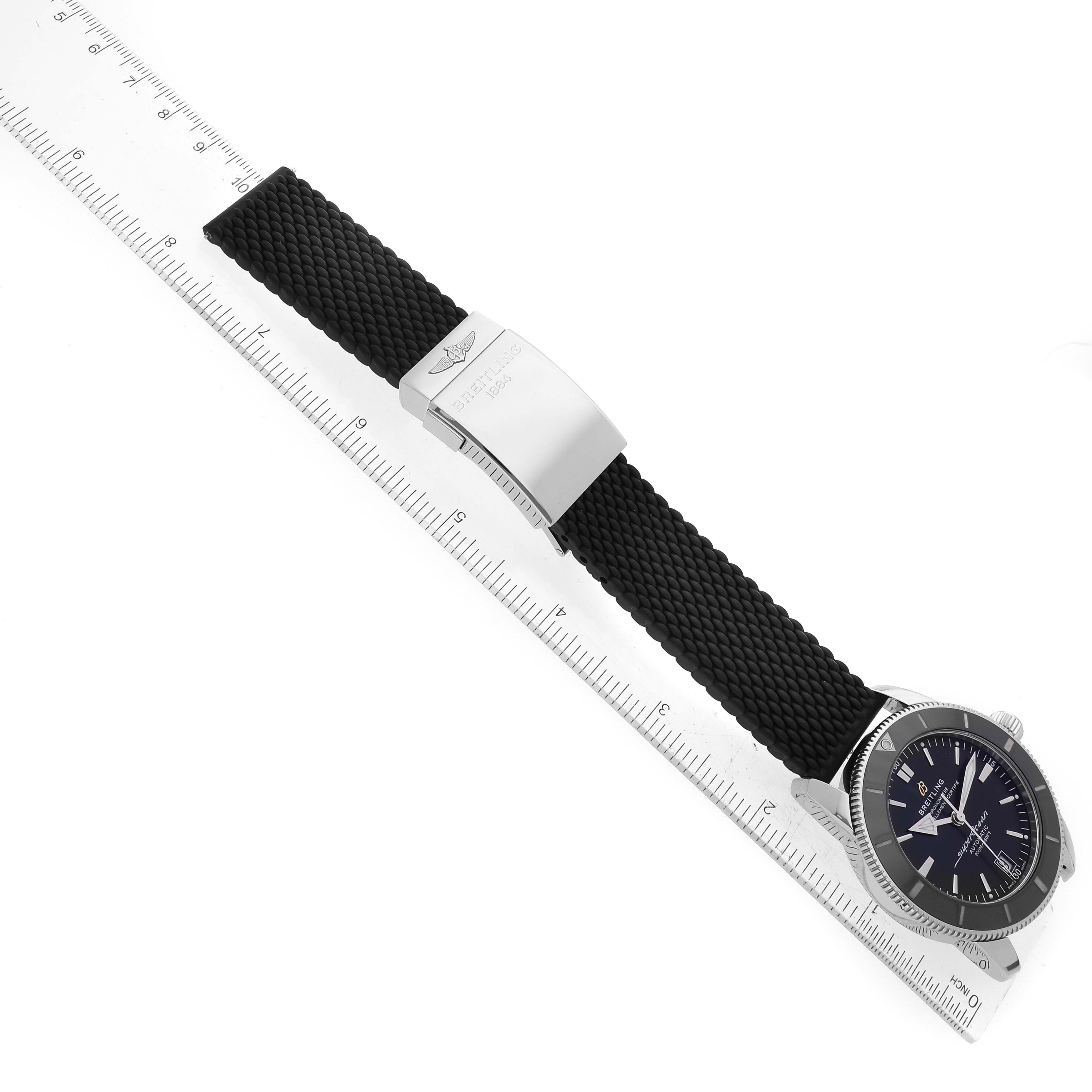 The Breitling Superocean AB2010 Men
s Stainless Steel Black Dial AB2010 Men
s Stainless Steel Black Dial watch is shown at a slight angle displaying the face, crown, buckle, and black strap alongside a ruler.