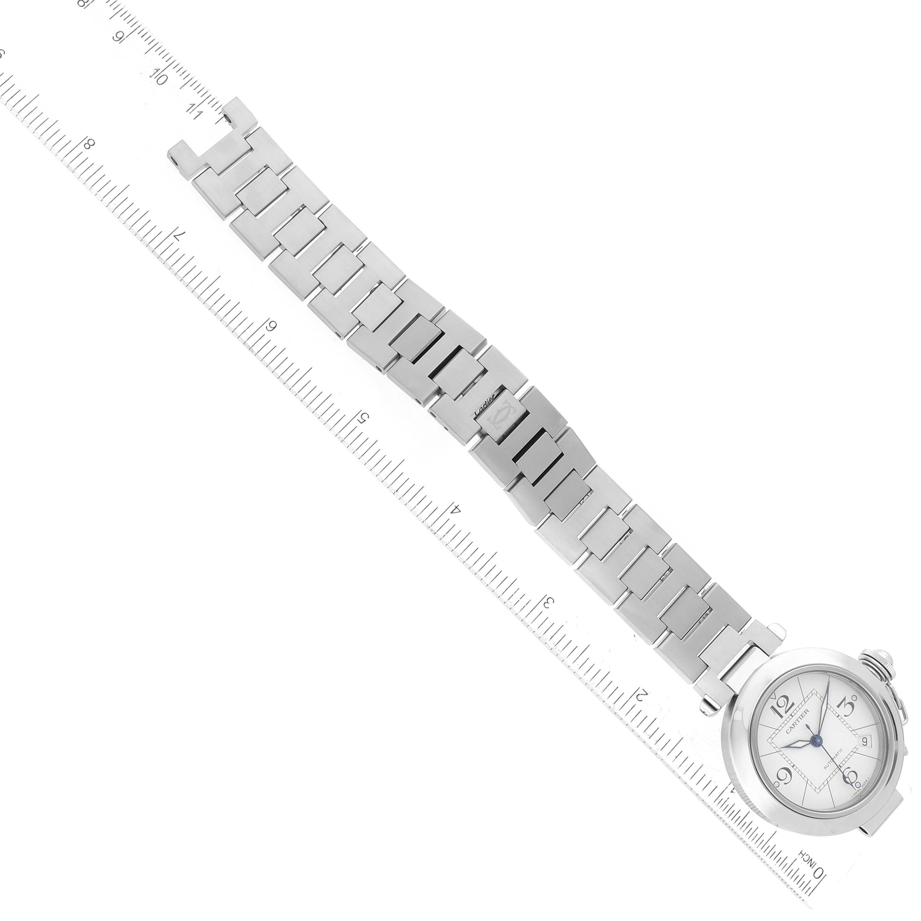 The image shows the entire Cartier Pasha W31074M7 Men's Stainless Steel White Dial W31074M7 Men's Stainless Steel White Dial watch, including the face and metal bracelet, laid next to a ruler for scale.