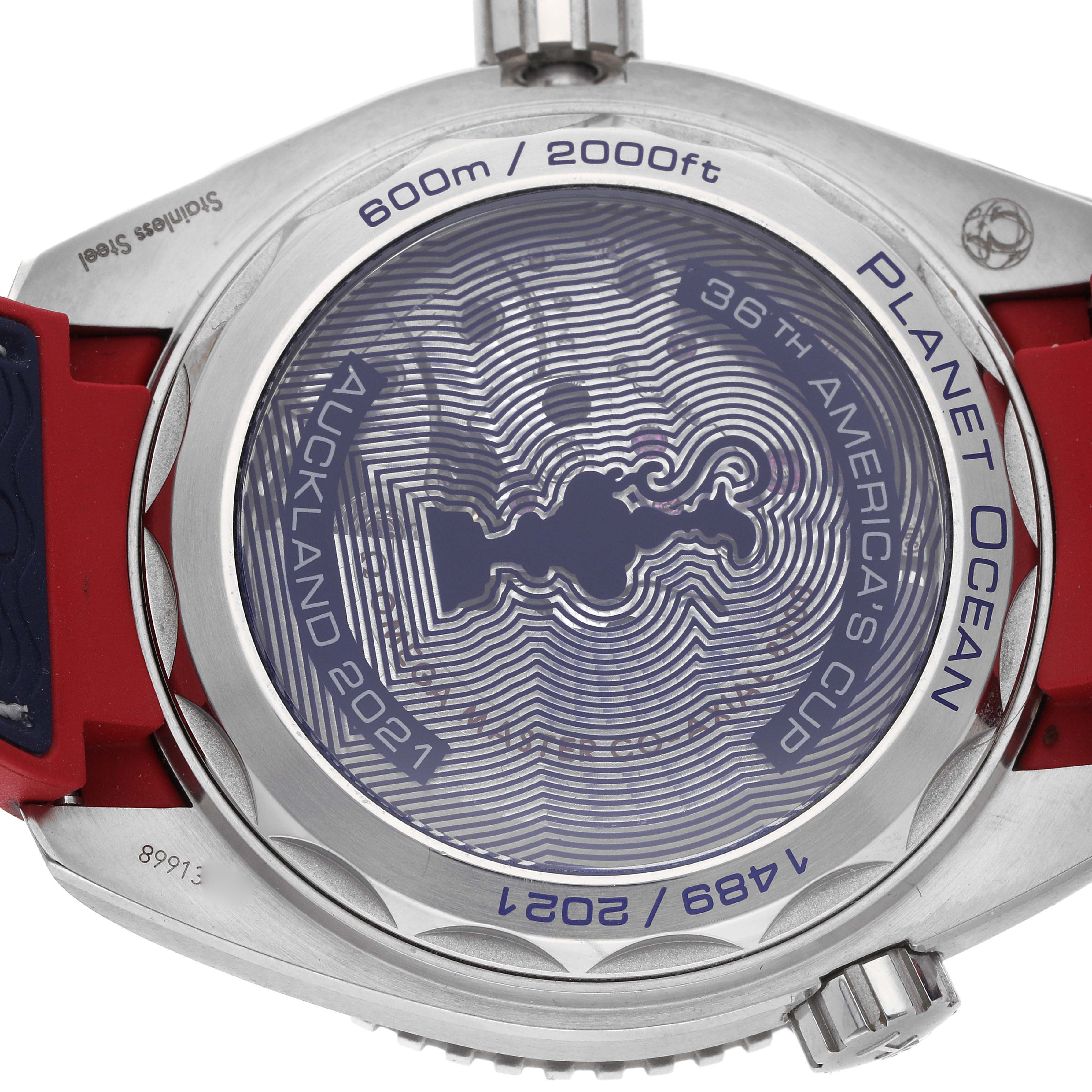The image shows the back of the Omega Planet Ocean 215.32.43.21.04.001 Men
s Stainless Steel White Dial watch, displaying engravings and markings with a metal case and red strap.