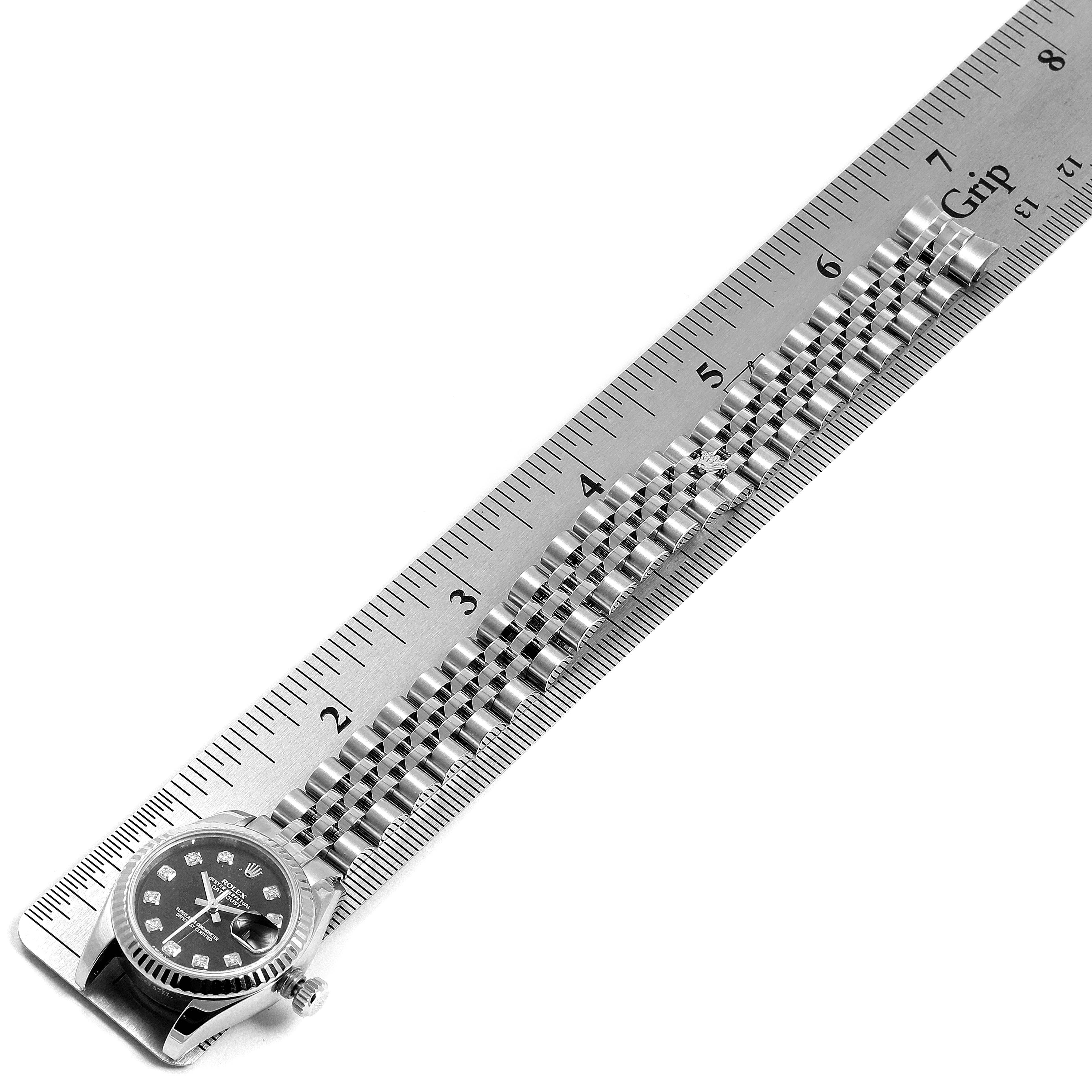 The image shows a Rolex Datejust 179174  Women's Stainless Steel Black Dial 179174  Women's Stainless Steel Black Dial watch placed diagonally alongside a ruler, highlighting its bracelet and part of the case.