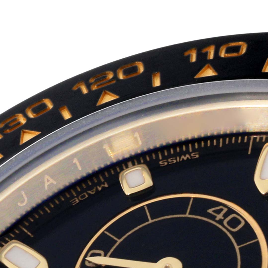 This close-up of the Rolex Daytona 116518L Men's Yellow Gold Black Dial 116518L Men's Yellow Gold Black Dial watch shows the bezel with tachymeter scale and part of the dial with markers and hands.