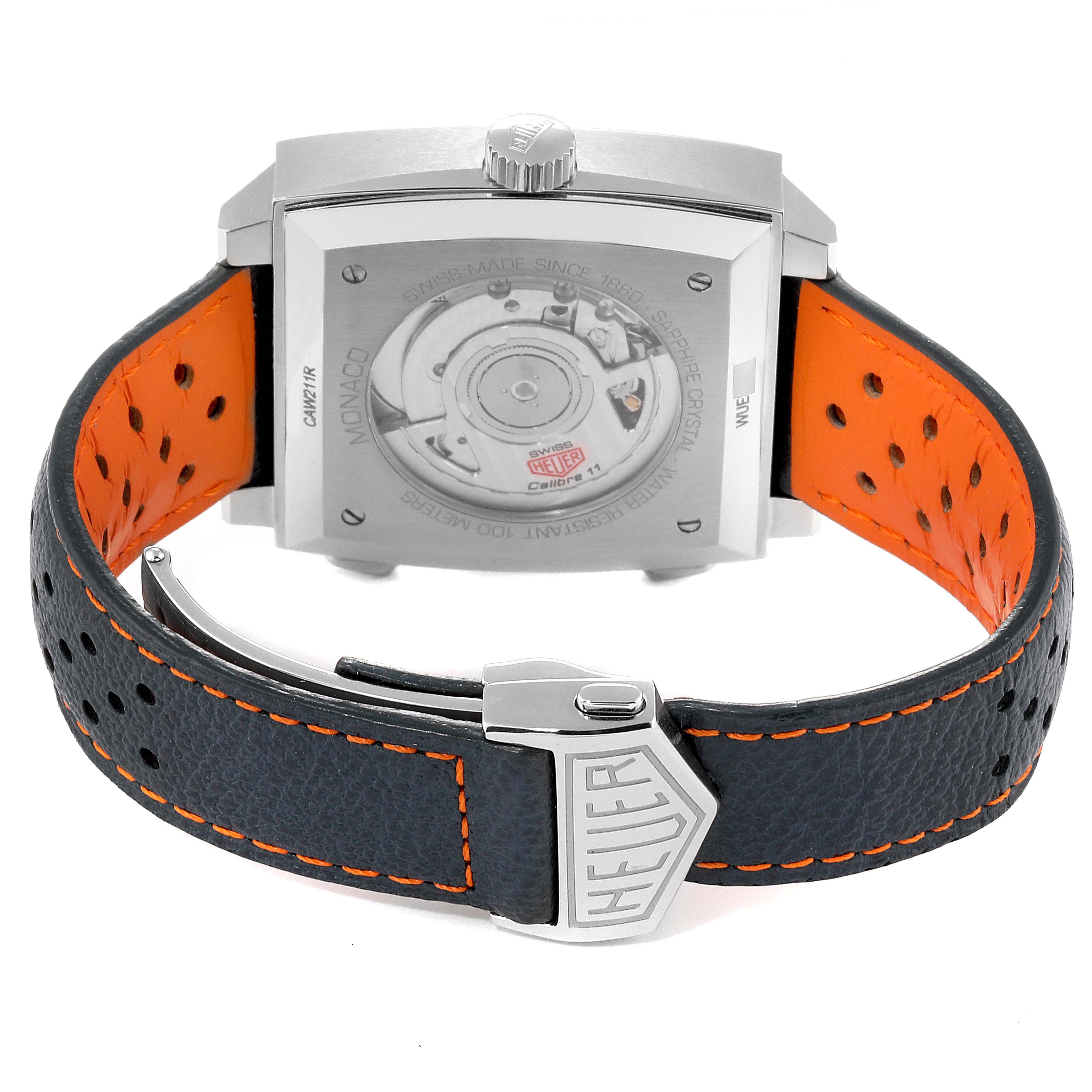 The image shows the back view of a Tag Heuer Monaco CAW211R.FC6401 Men's Stainless Steel Blue Dial CAW211R.FC6401 Men's Stainless Steel Blue Dial watch, featuring its mechanism through a transparent case back and a perforated strap with orange lining.