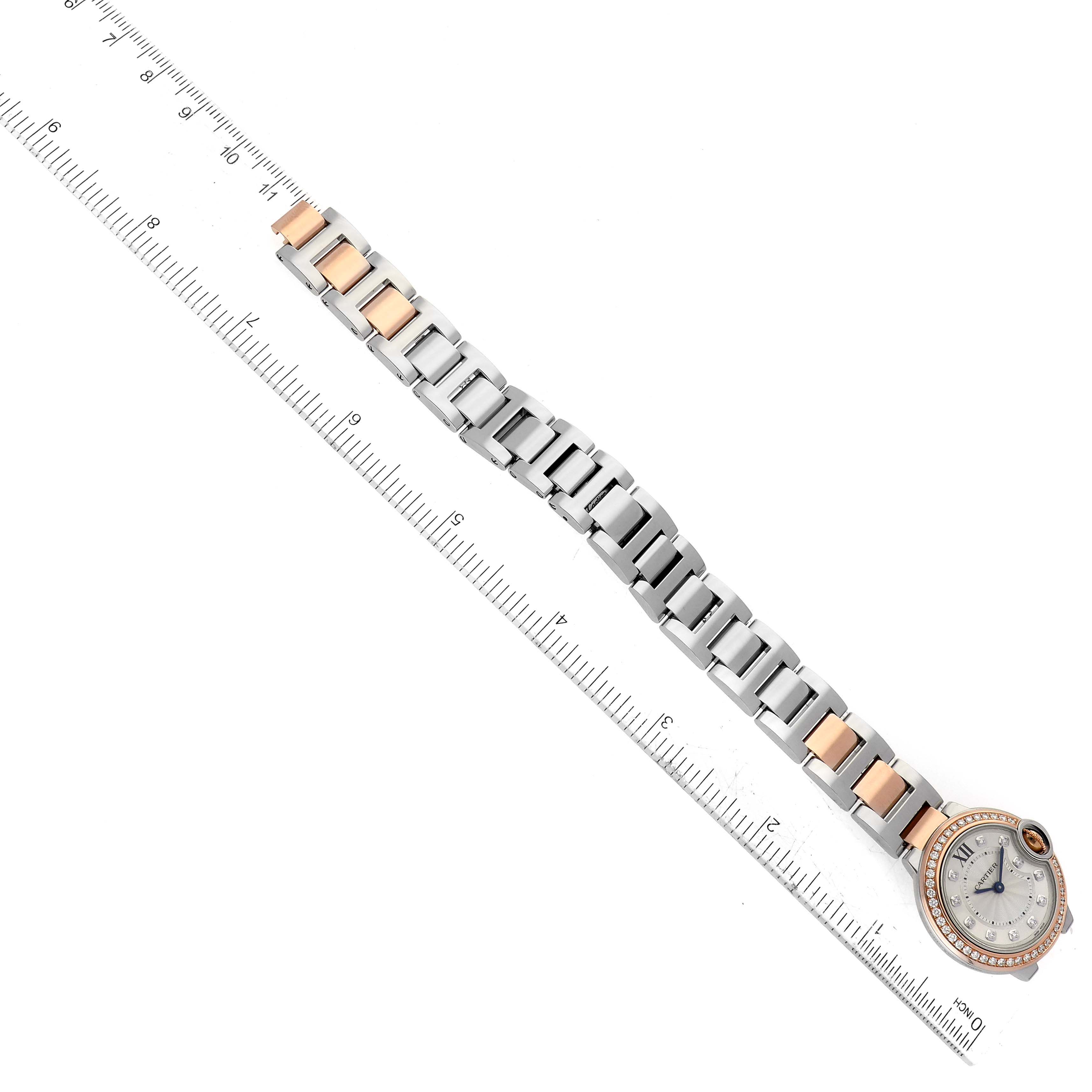 The image shows a Ballon Bleu de Cartier watch laid flat at an angle with a ruler, highlighting its full band and face.