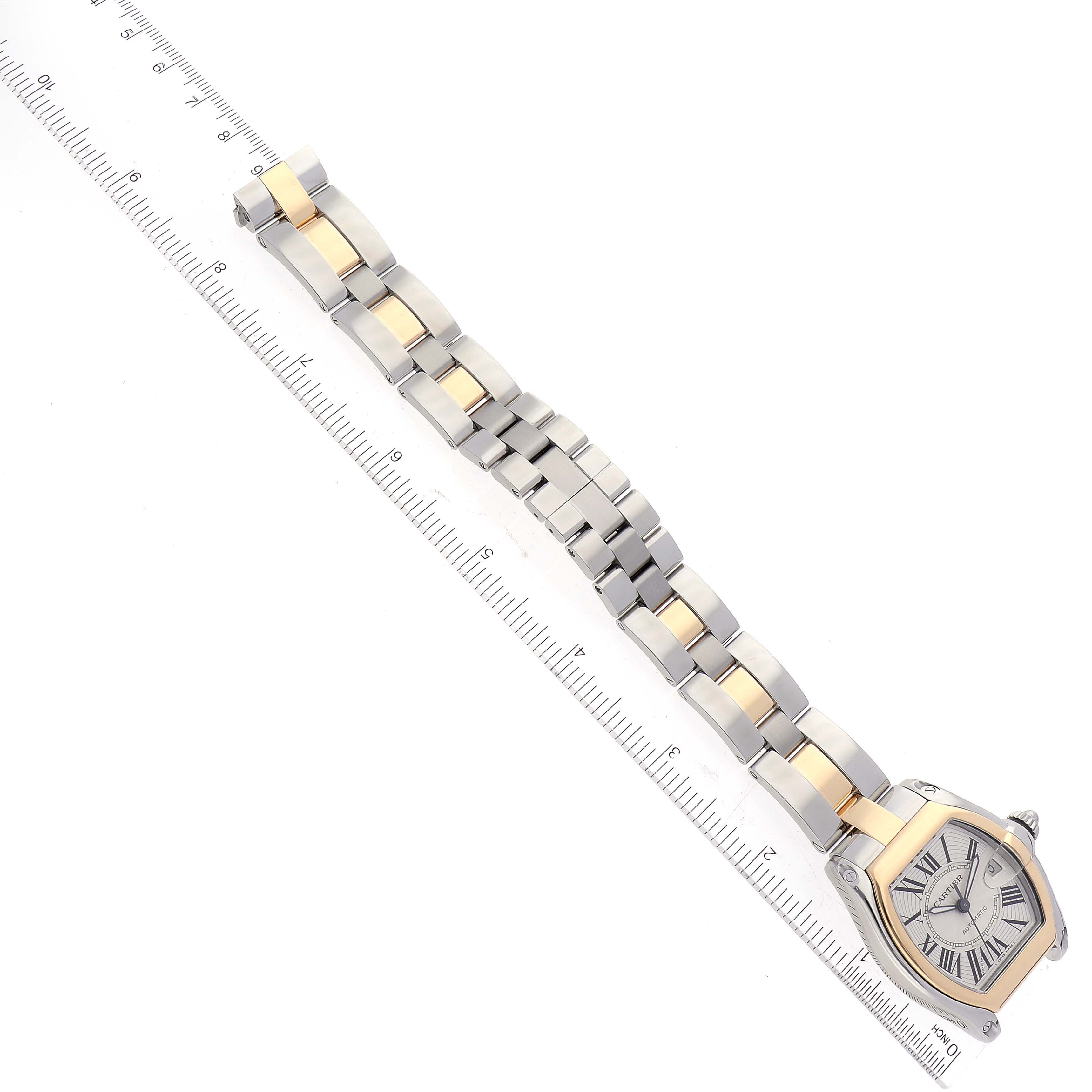 This image shows the Cartier Roadster W62031Y4 Men
s Steel and Gold (two tone) Silver Dial W62031Y4 Men
s Steel and Gold (two tone) Silver Dial watch and its bracelet in a top-down view next to a measuring ruler.