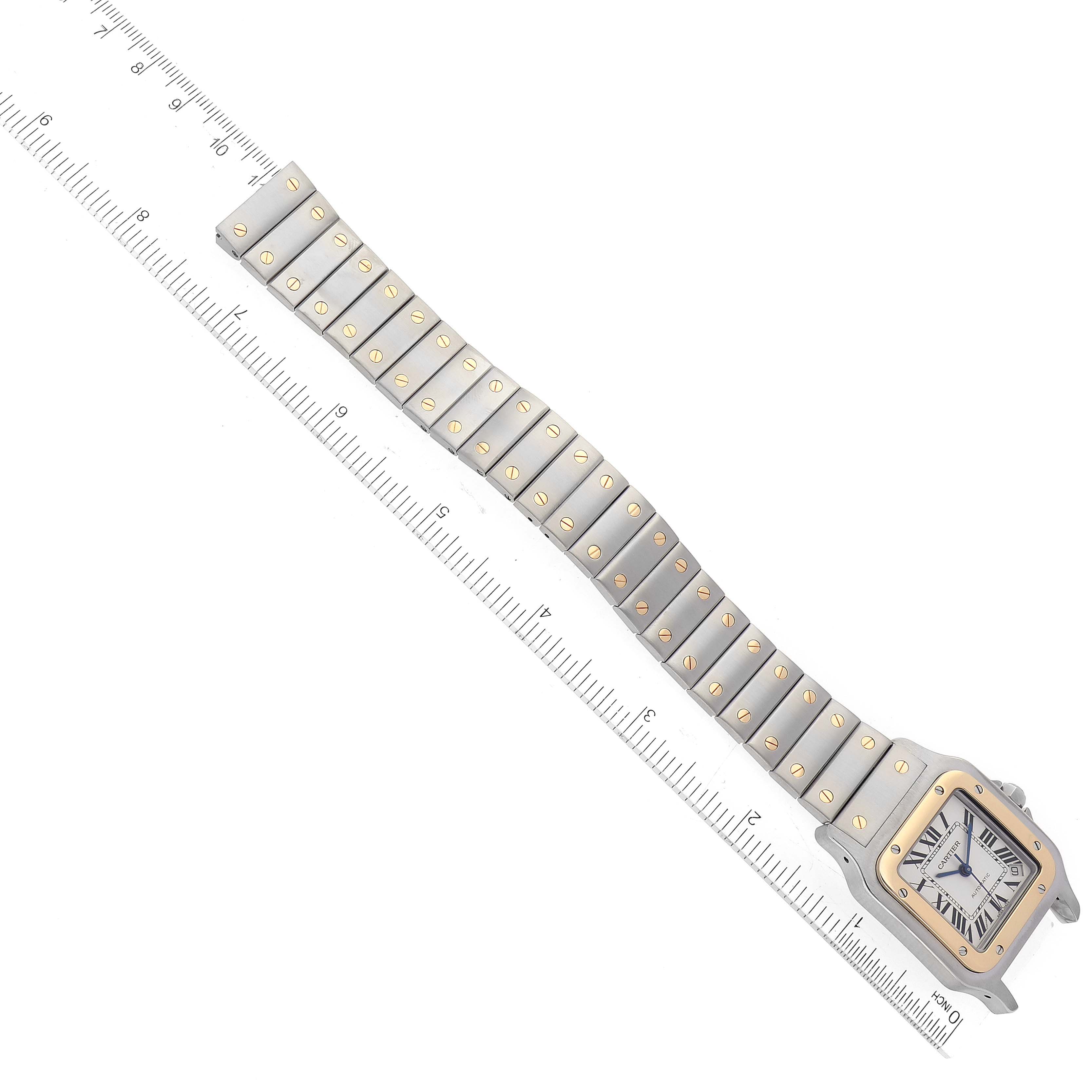 This image shows the Cartier Santos W20099C4 Men
s Steel and Gold (two tone) Silver Dial W20099C4 Men
s Steel and Gold (two tone) Silver Dial watch face and full bracelet from a top-down angle next to a ruler.