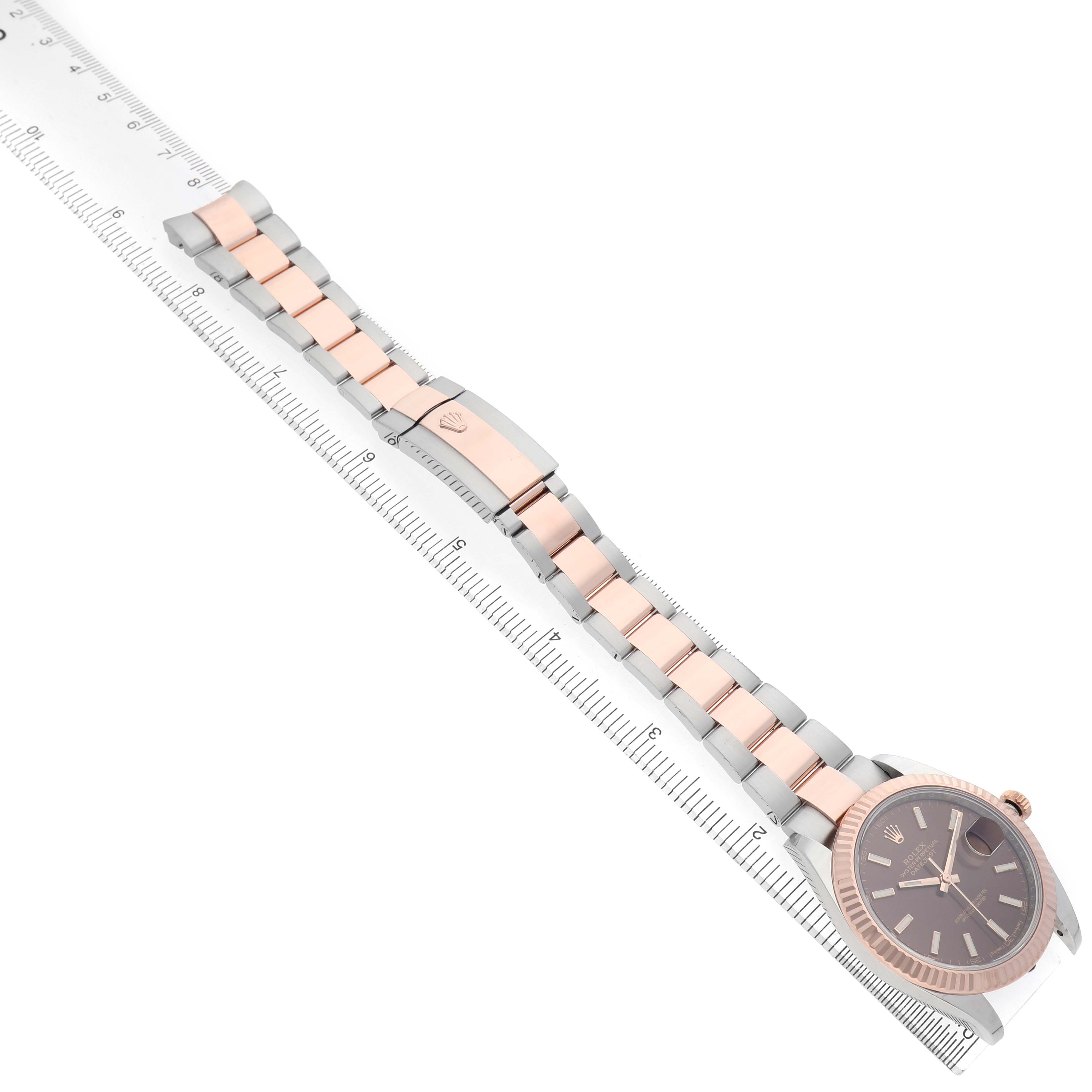 The Rolex Datejust 41 126331 Men's Steel and Gold (two tone) Brown Dial is shown from an overhead angle, featuring the watch face, bracelet, and clasp beside a ruler for scale.