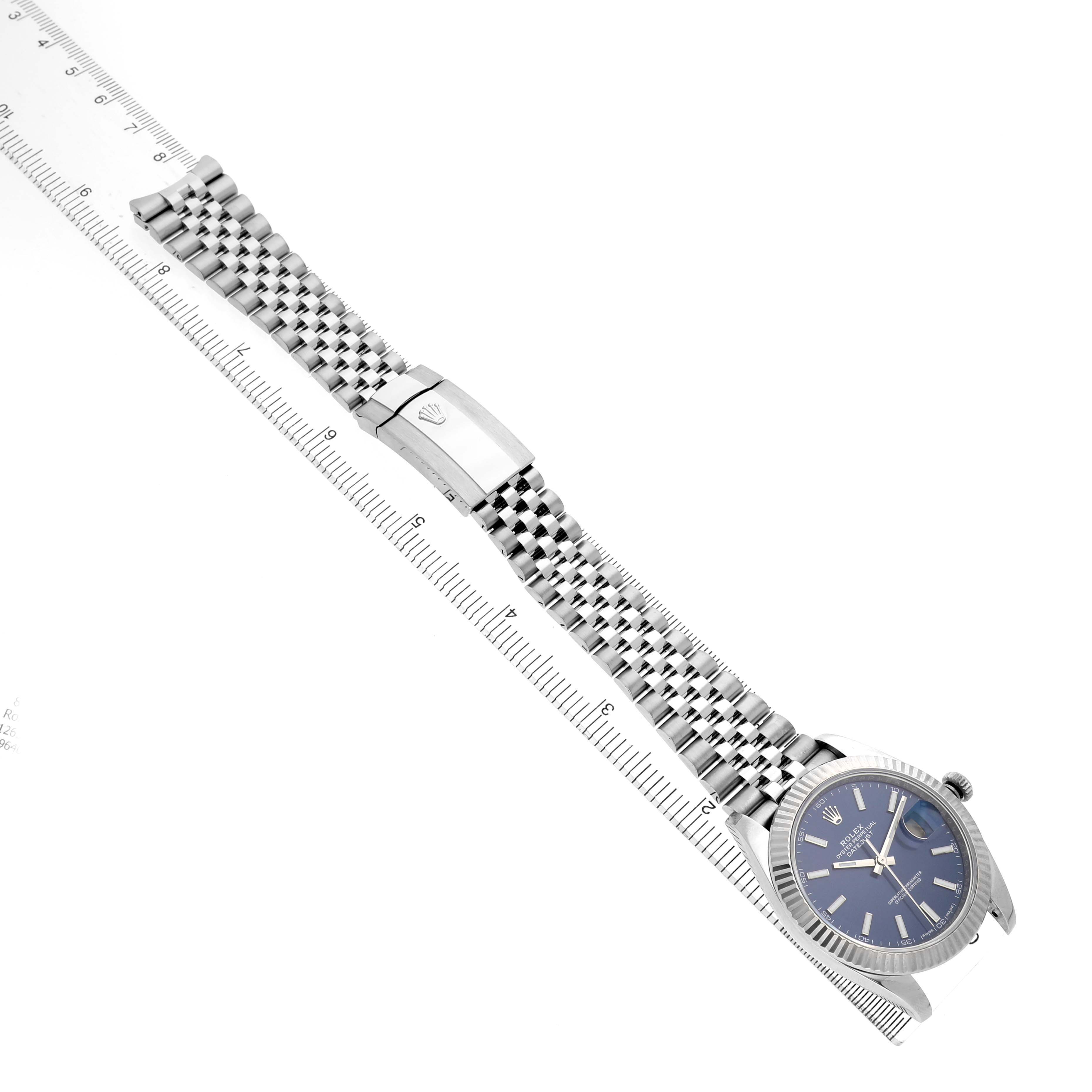 The Rolex Datejust 41 126334 Men's Stainless Steel Blue Dial watch is shown from a top-down angle, displaying its full bracelet and clasp alongside a ruler.