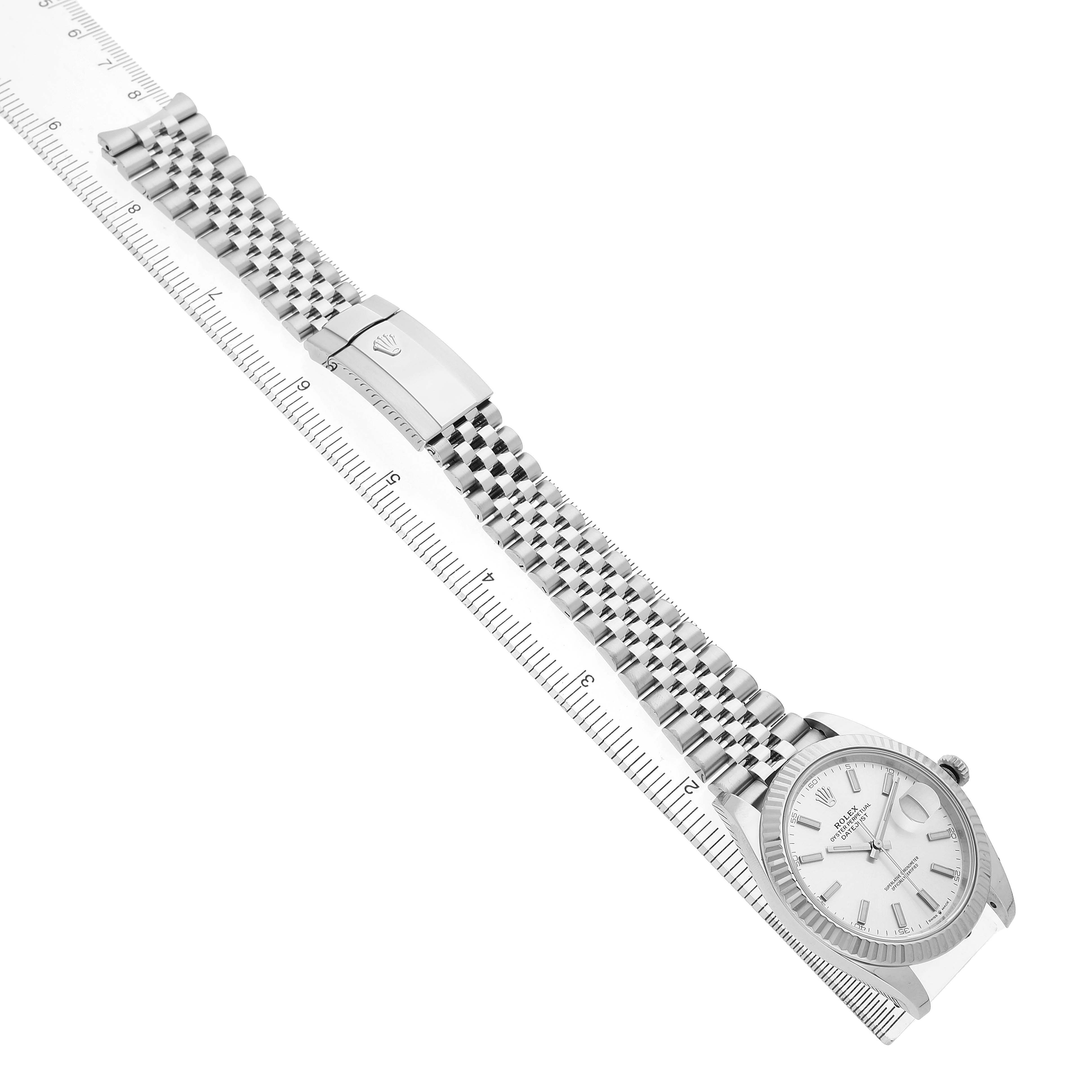 The Rolex Datejust 41 126334 Men's Stainless Steel Silver Dial is shown with an angled view displaying the watch face, Jubilee bracelet, and clasp near a ruler.
