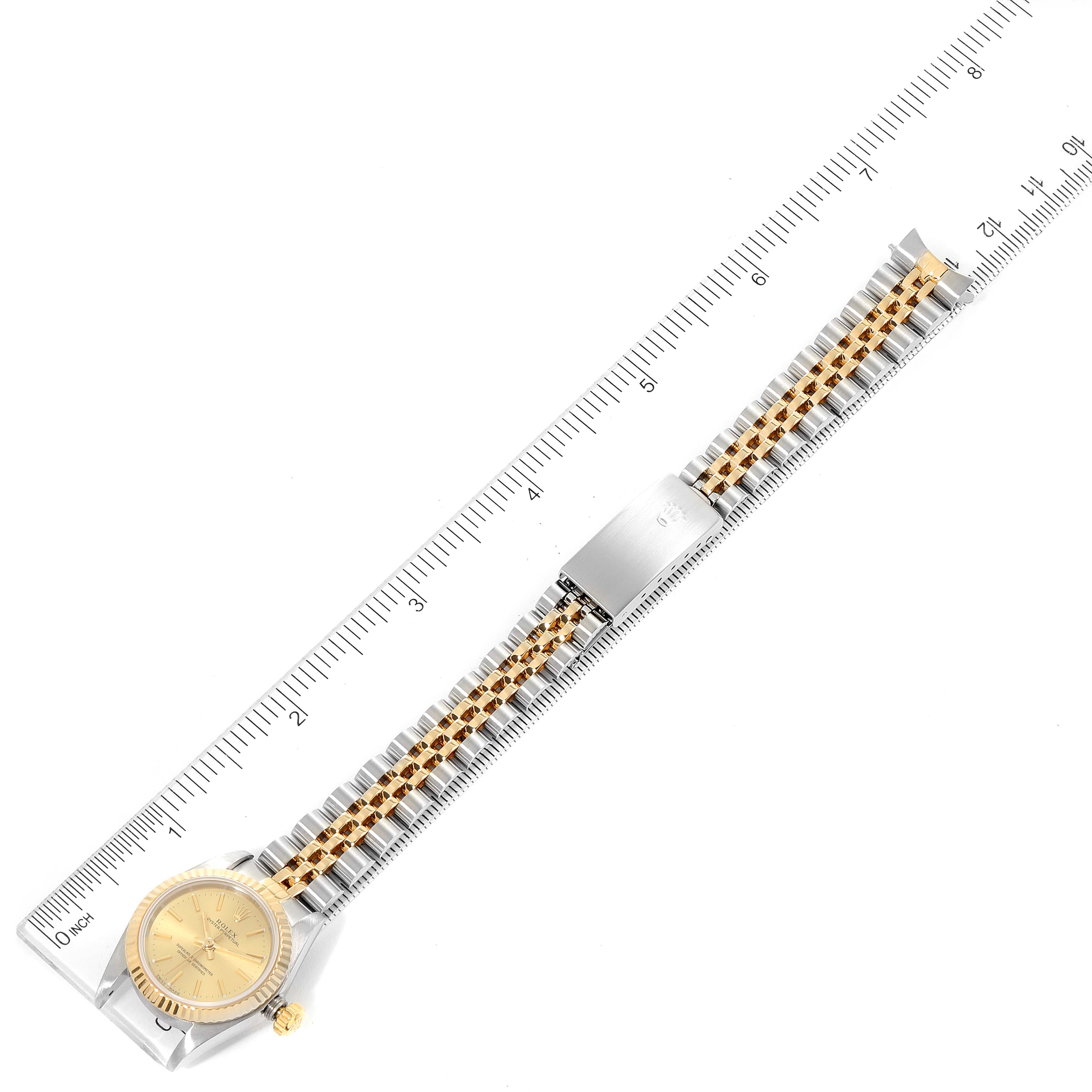 The image shows a top-down view of a Rolex Oyster Perpetual 76193 Women
s Steel and Gold (two tone) Champagne Dial 76193 Women
s Steel and Gold (two tone) Champagne Dial watch laid on a ruler, highlighting its gold and silver bracelet and dial.