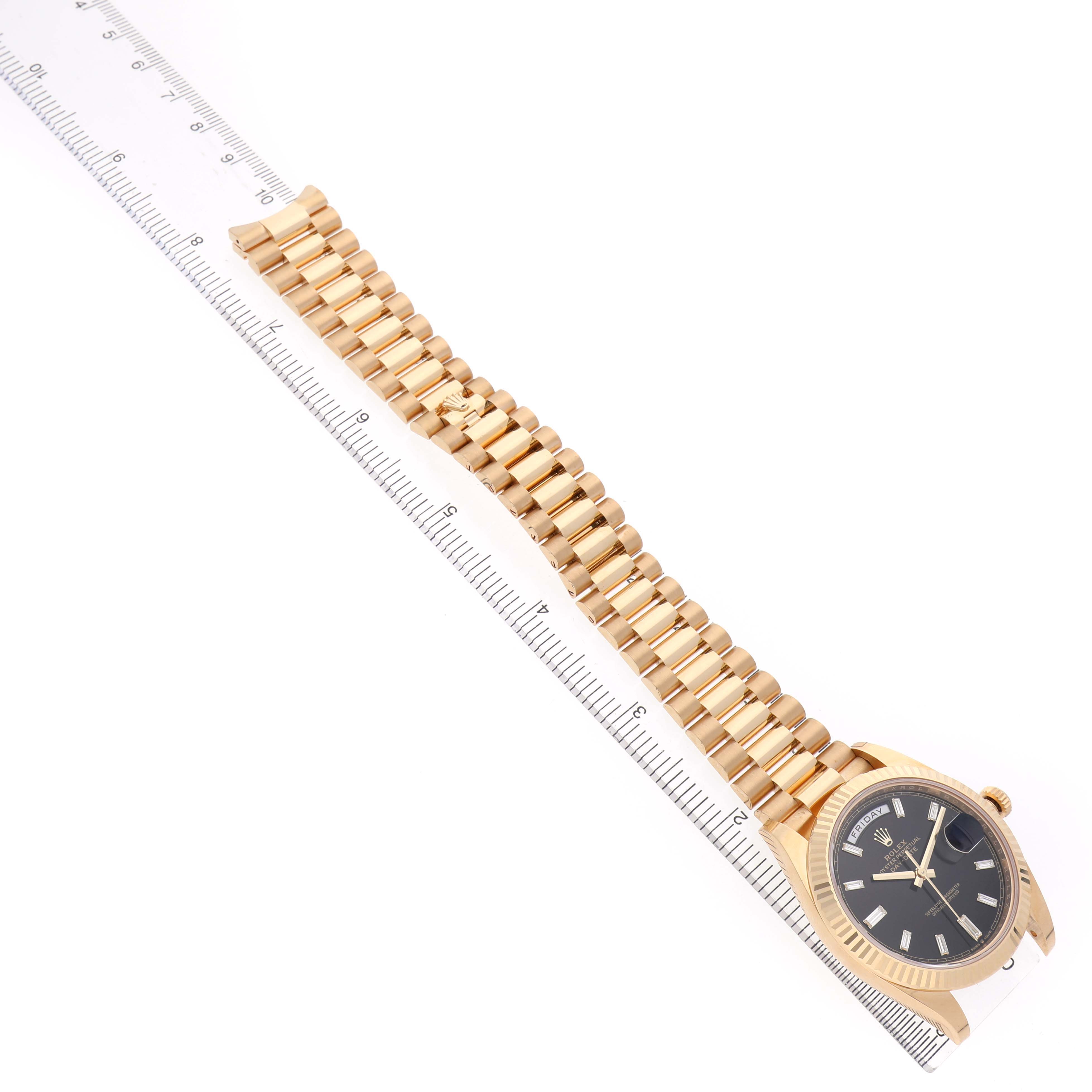 The Rolex President 228238 Men's Yellow Gold Black Dial watch is shown from a top-down angle, highlighting the bracelet and watch face alongside a ruler for scale.