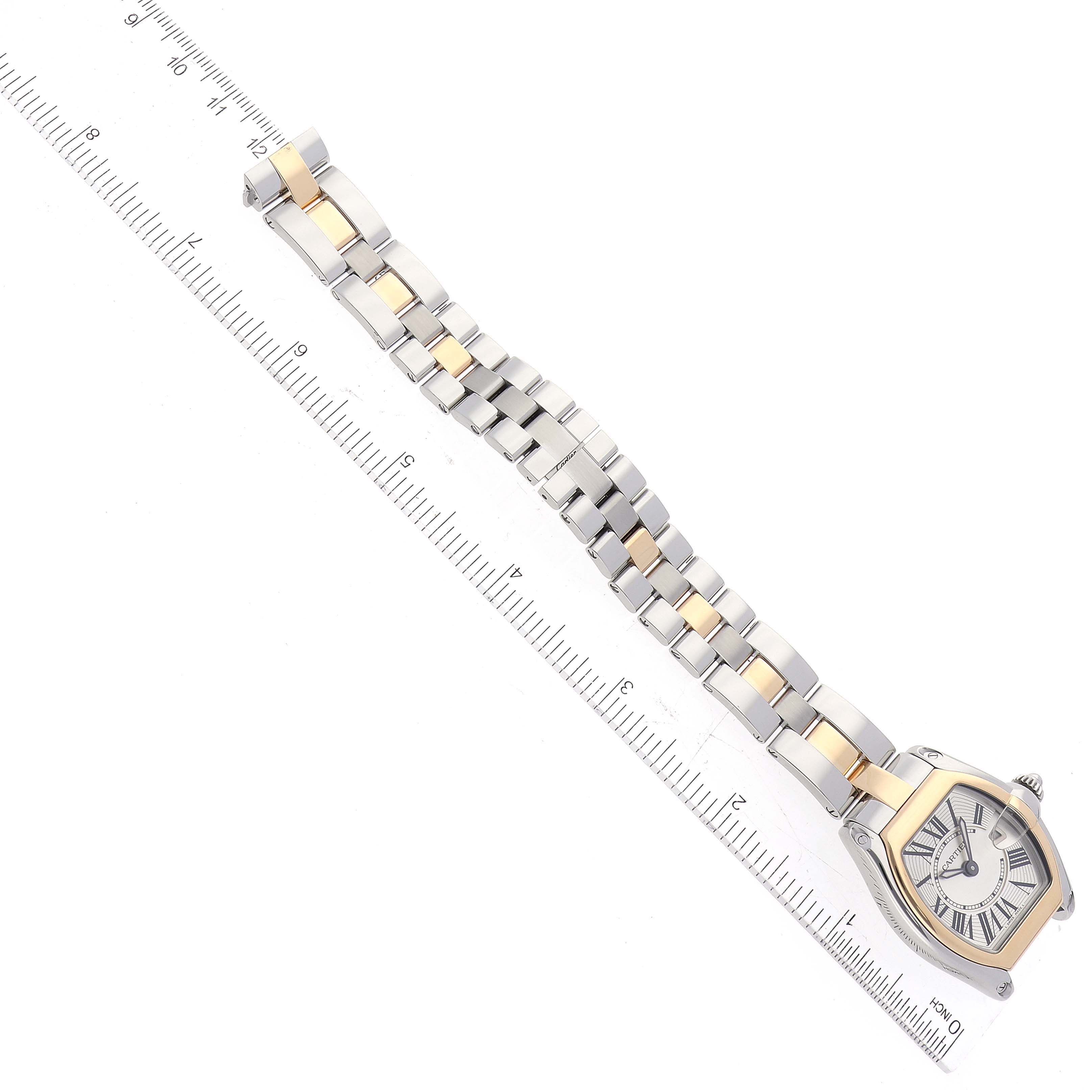 The Cartier Roadster W62026Y4 Women
s Steel and Gold (two tone) Silver Dial W62026Y4 Women
s Steel and Gold (two tone) Silver Dial watch is shown from a top-down angle, displaying the face, bezel, and full bracelet alongside a ruler.