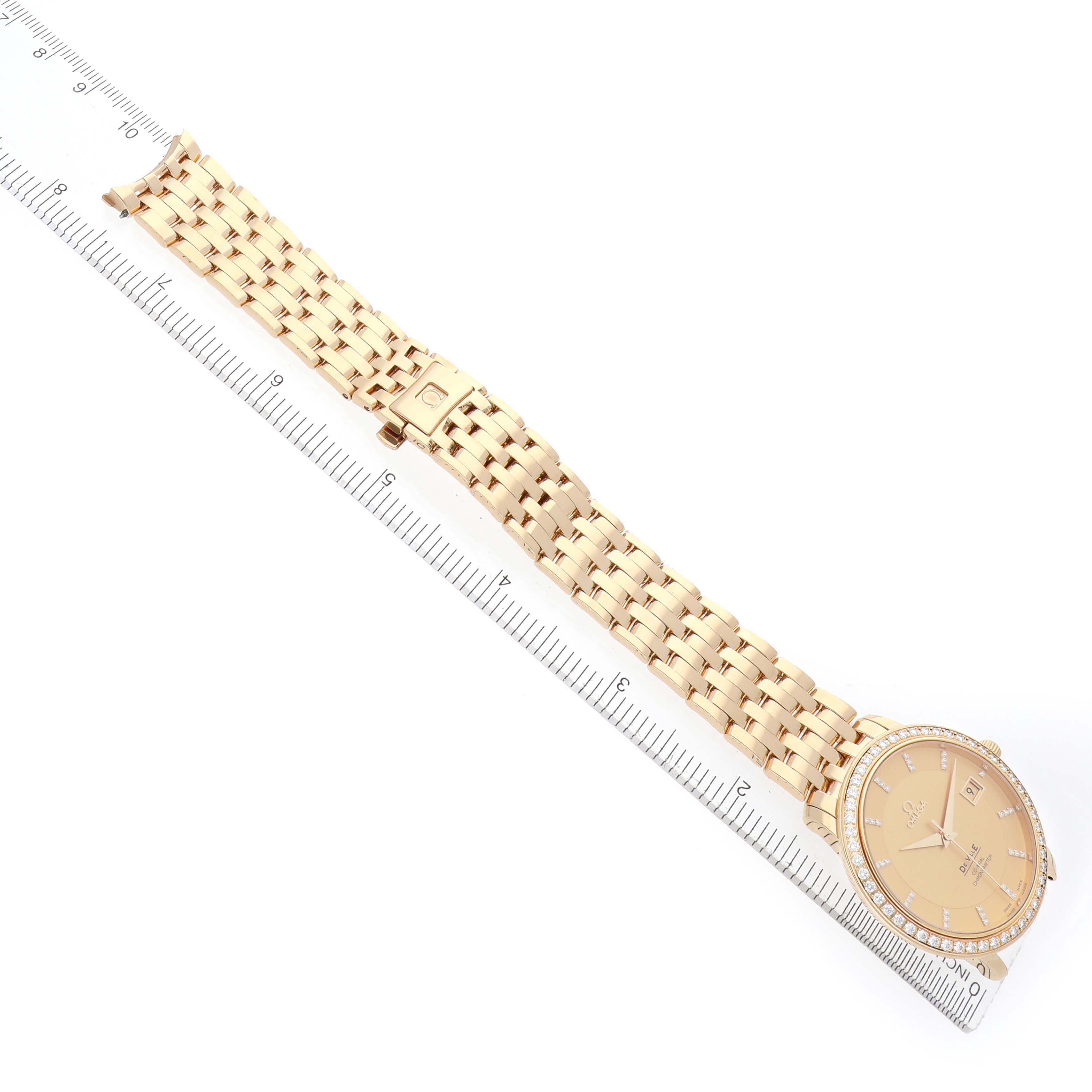 The Omega De Ville 413.58.37.20.58.001 Men's Yellow Gold Champagne Dial watch is displayed from an overhead angle, showing the entire band and face alongside a ruler.