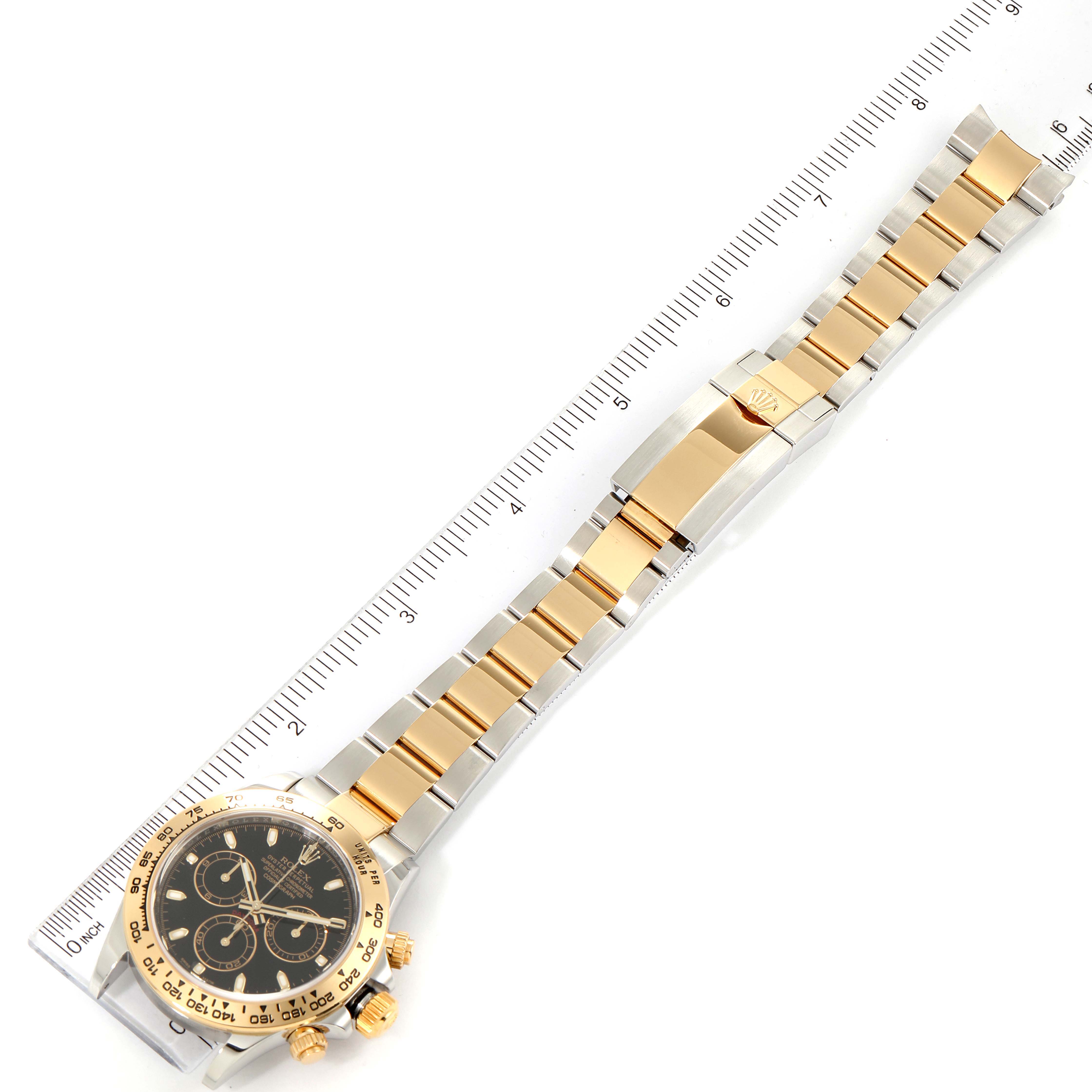 The image shows a Rolex Daytona 116503 Men's Steel and Gold (two tone) Black Dial 116503 Men's Steel and Gold (two tone) Black Dial watch laid flat with its gold and silver bracelet fully extended alongside a ruler.