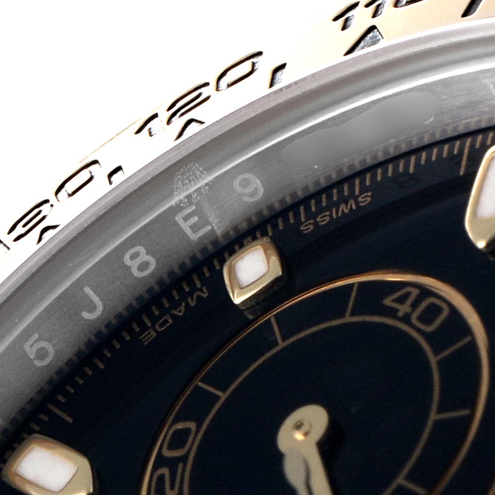The image shows a close-up angle of a Rolex Daytona 116503 Men's Steel and Gold (two tone) Black Dial 116503 Men's Steel and Gold (two tone) Black Dial watch, highlighting part of the bezel and the inner dial with markers.