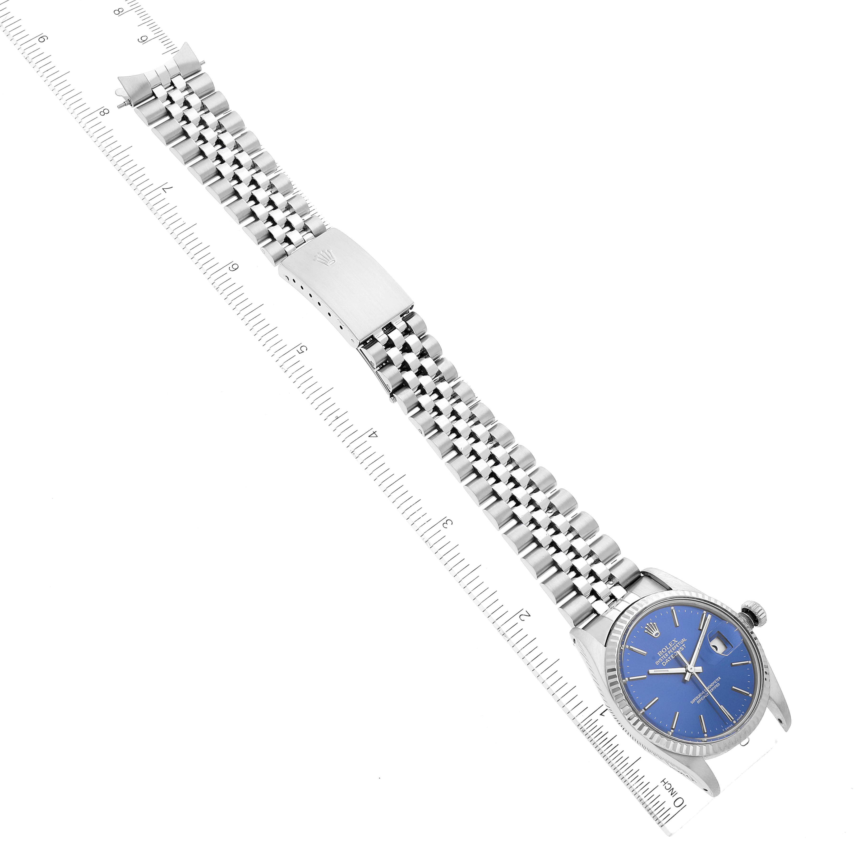 The image shows a side angle of a Rolex Vintage Collection 16030 Men's Stainless Steel Blue Dial 16030 Men's Stainless Steel Blue Dial watch with a blue dial and a metal bracelet laid out straight beside a ruler.