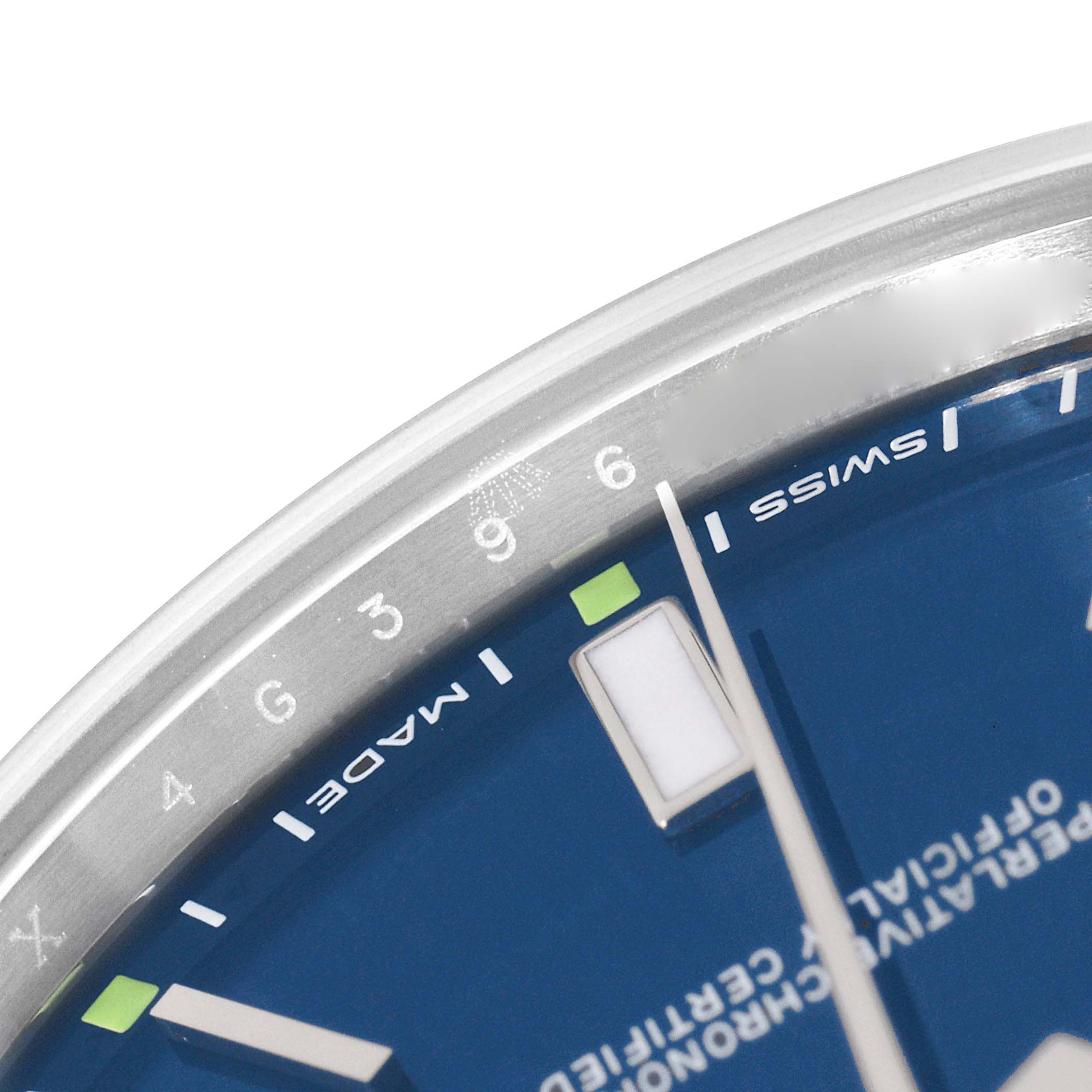 The image shows a close-up of the dial of a Rolex Oyster Perpetual 114300 Men's Stainless Steel Blue Dial 114300 Men's Stainless Steel Blue Dial watch, displaying the 9 o'clock marker and part of the hour and minute hands.